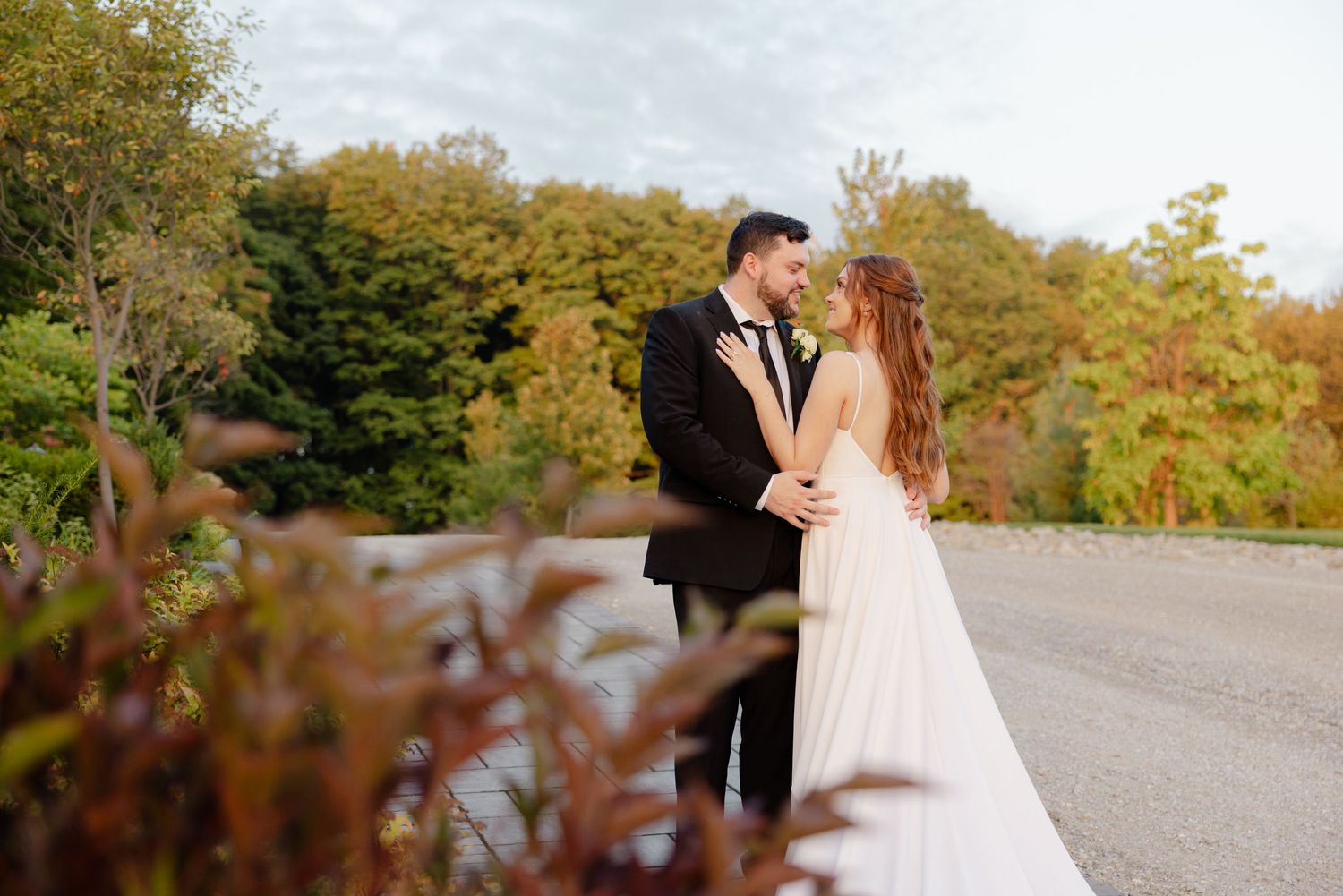 Wedding couple shares an intimate moment on stone pavement with fall foliage in background.