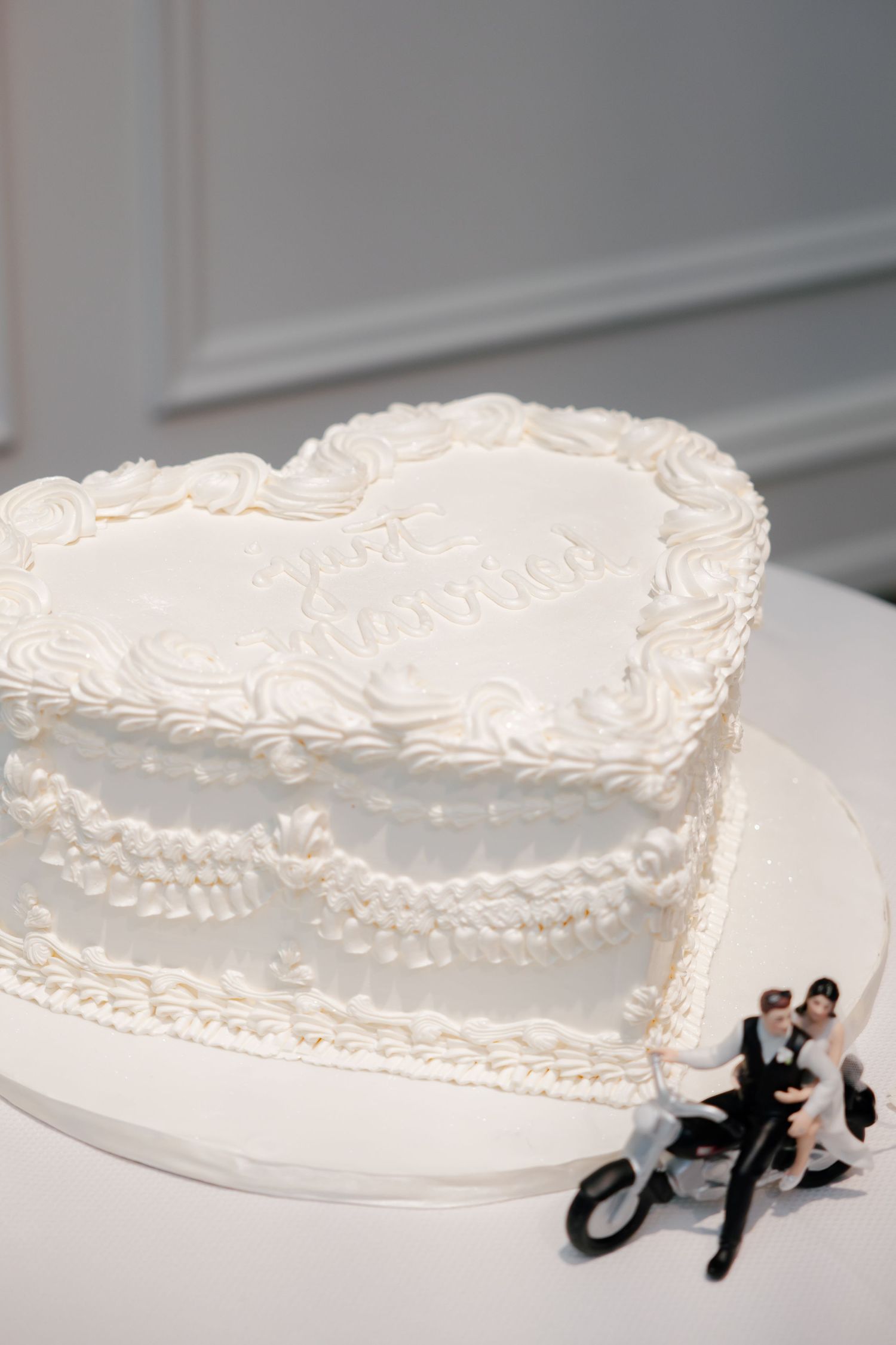 Heart-shaped white wedding cake decorated with piped details and motorcycle cake topper.