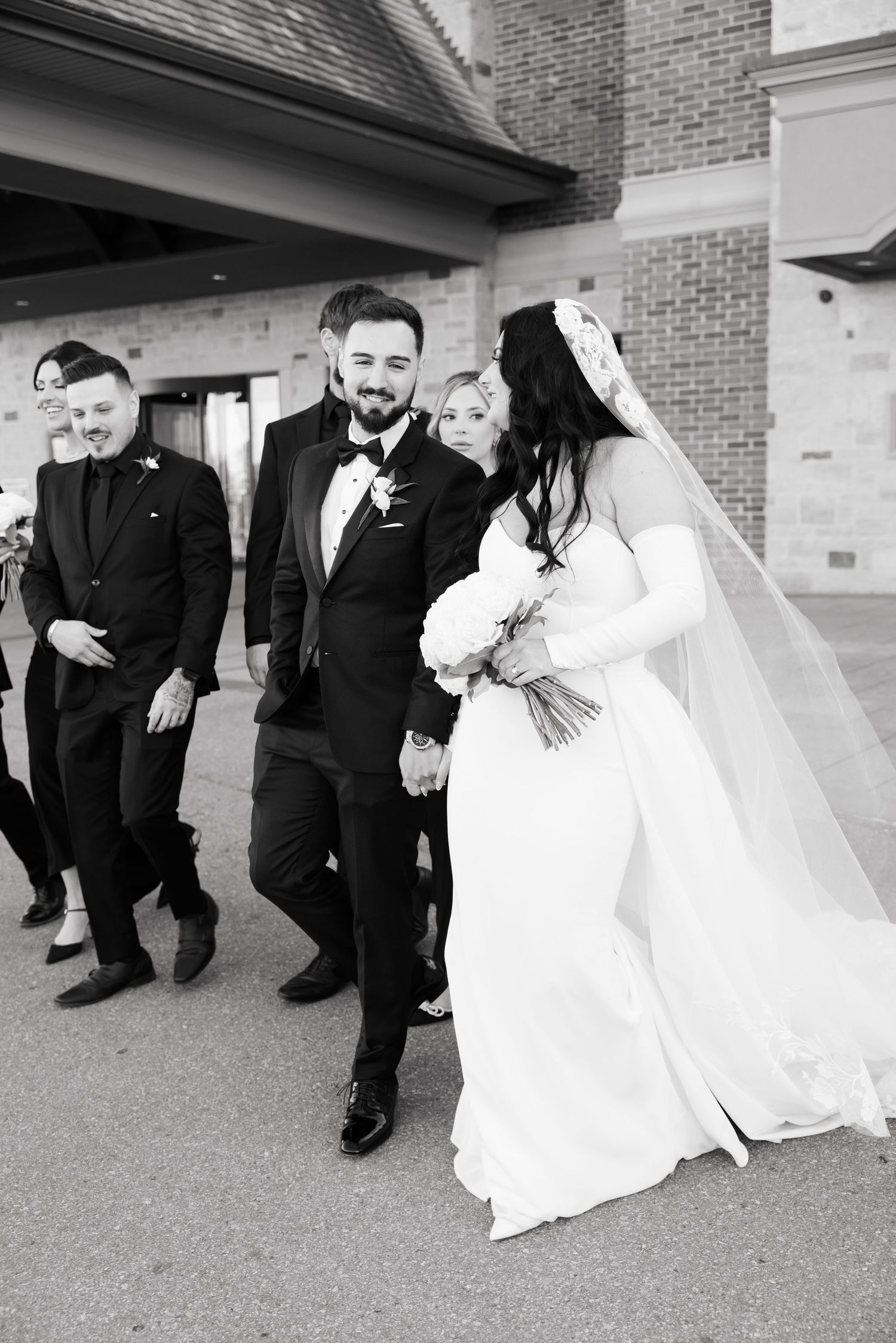 Wedding couple shares a candid moment with wedding party members in black attire.