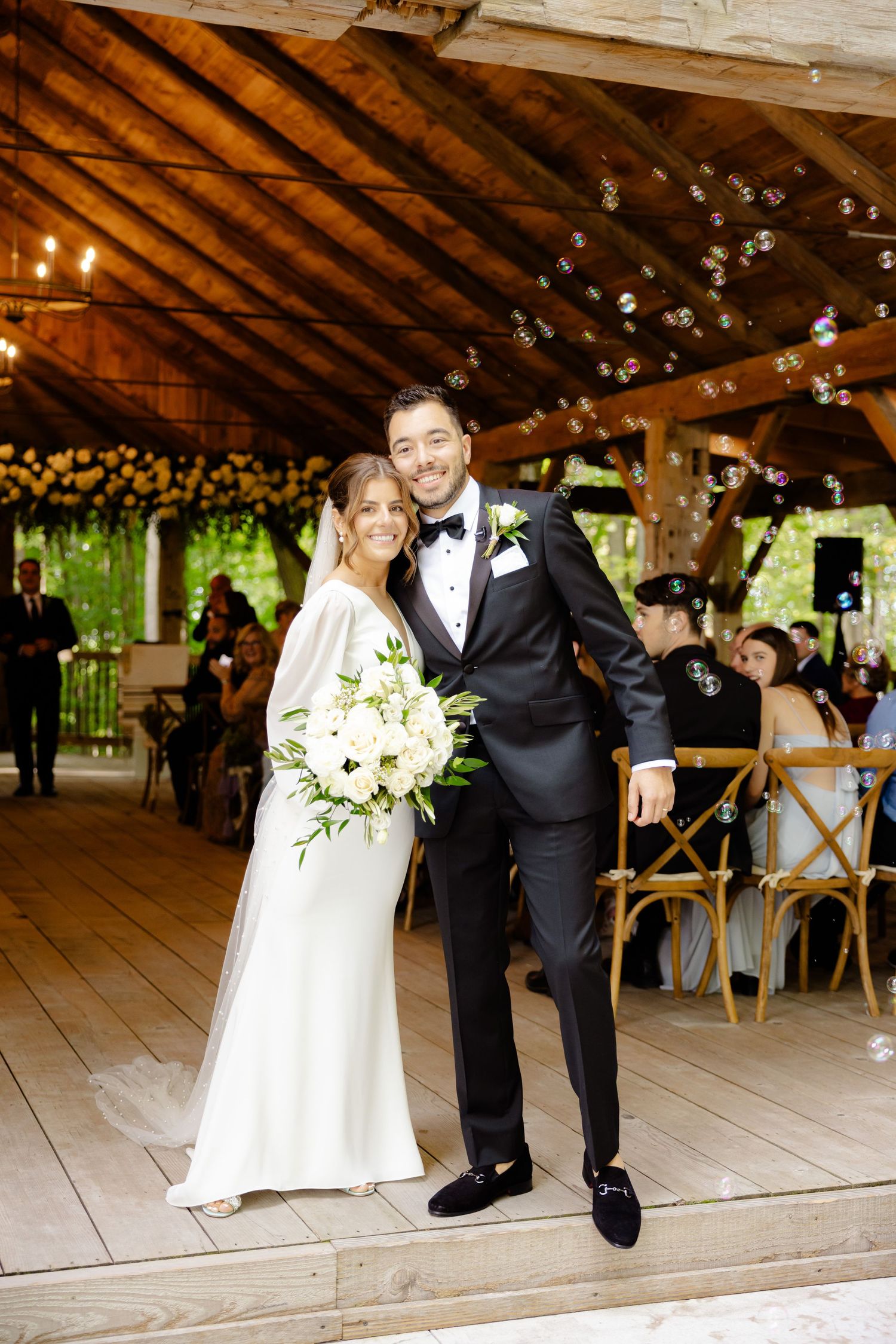 A wedding celebration in a rustic wooden pavilion decorated with string lights and white flowers.