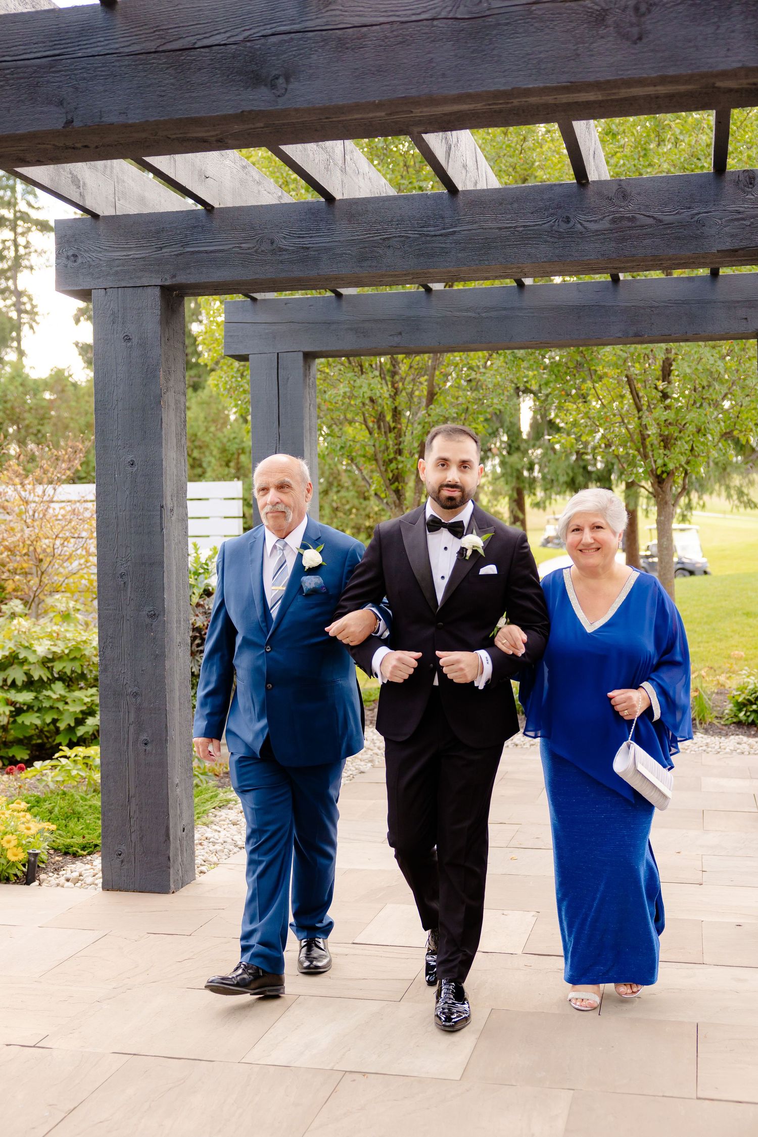 A formal processional under a wooden pergola during an outdoor wedding event.