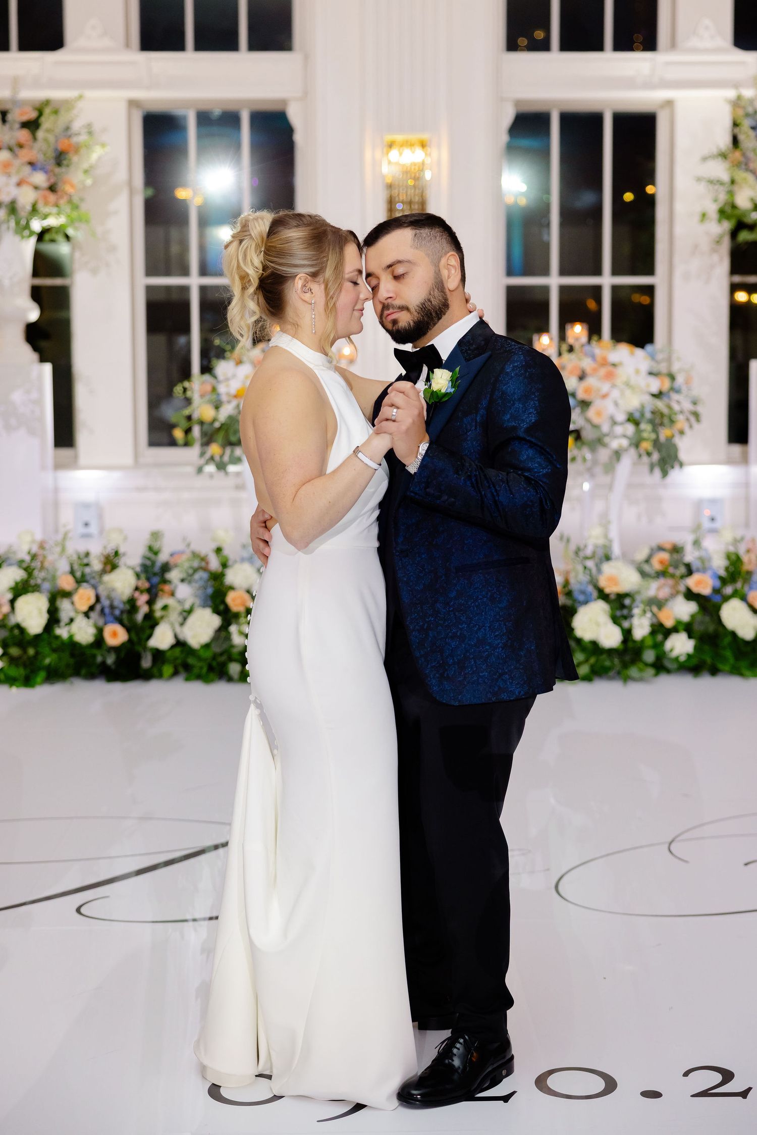 Couple dancing in an elegant white ballroom with romantic floral decorations.