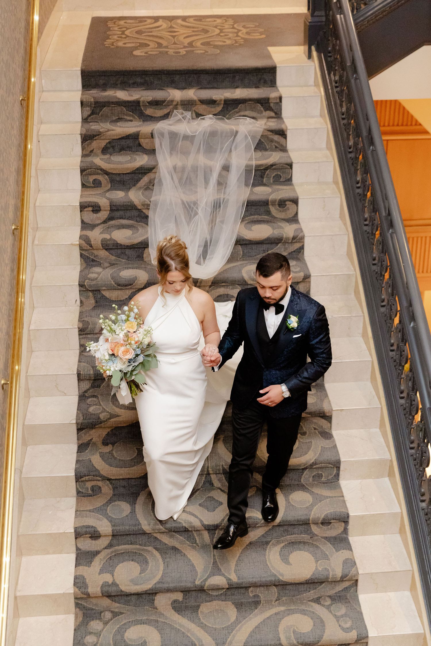 A couple walks down carpeted stairs with decorative patterns during their wedding day.