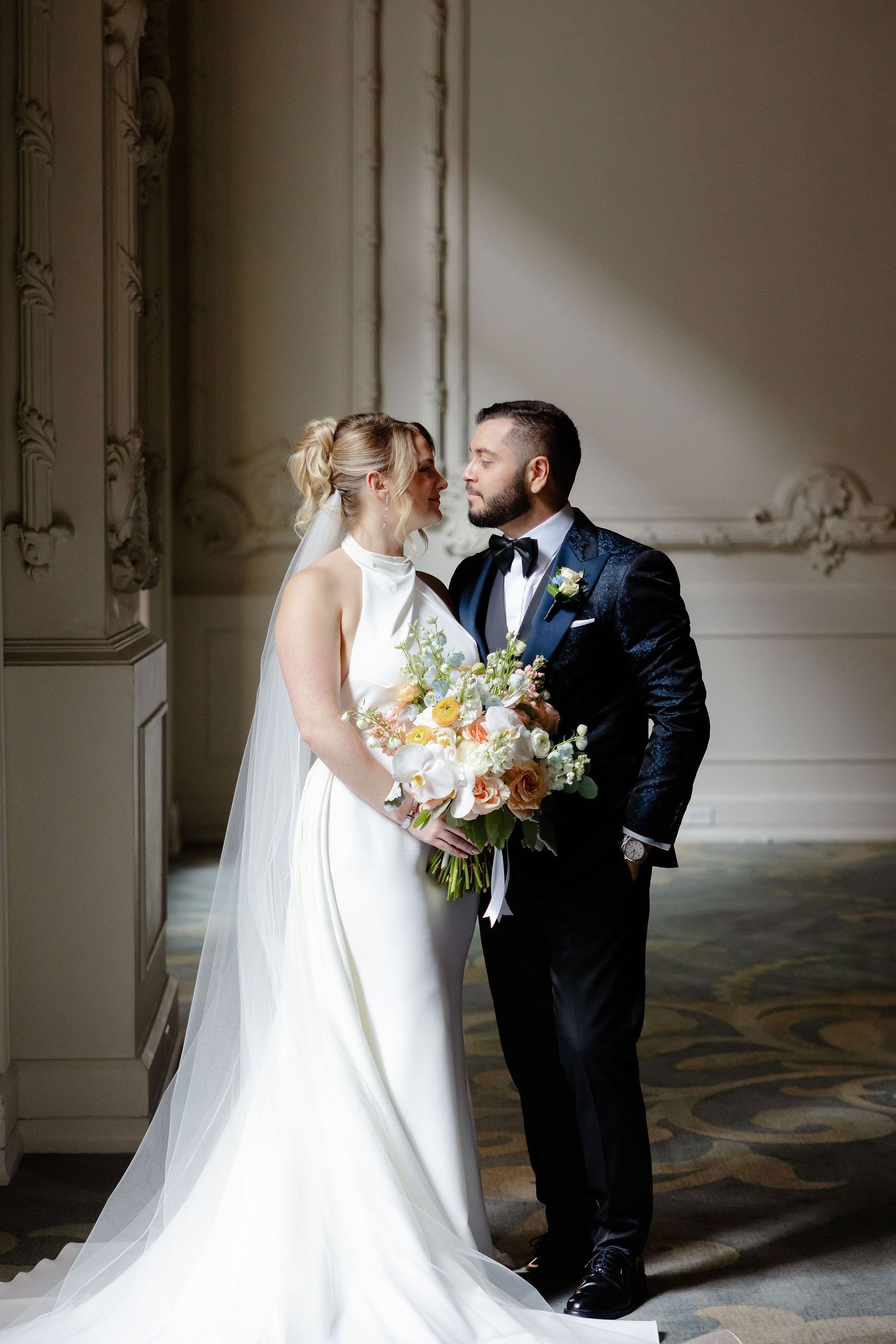 Romantic first look wedding moment in an elegant room with ornate moldings and flowing bridal gown.
