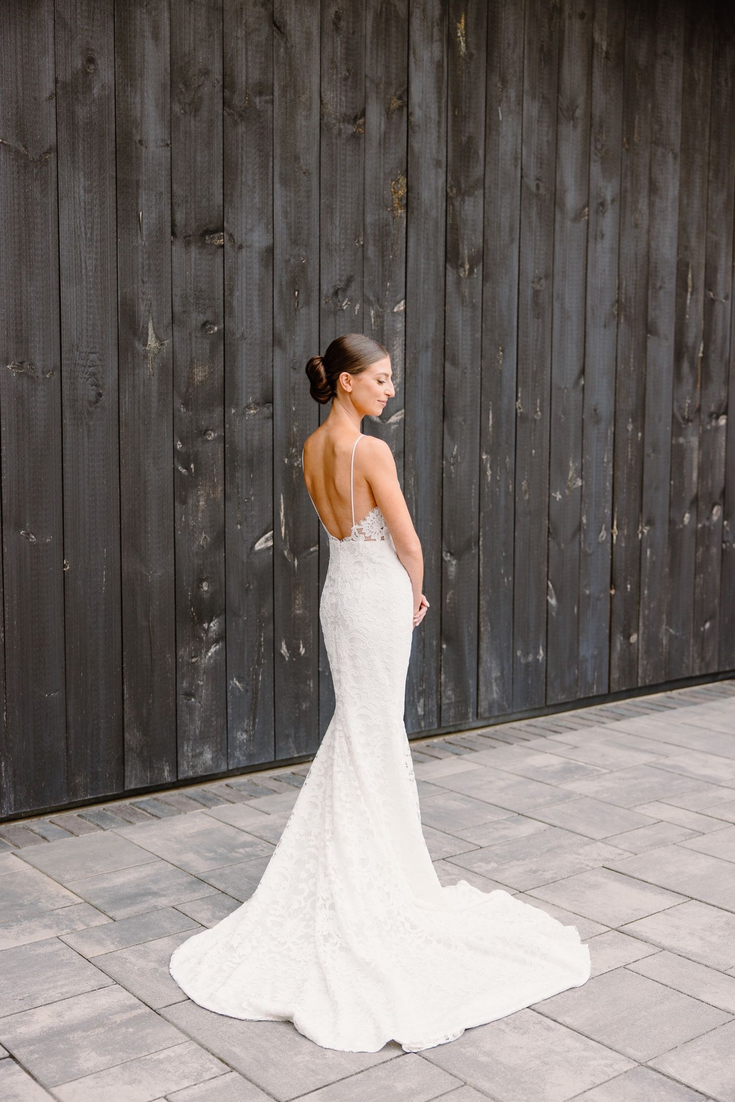 Elegant fitted wedding dress with low back and long train against dark wood backdrop.