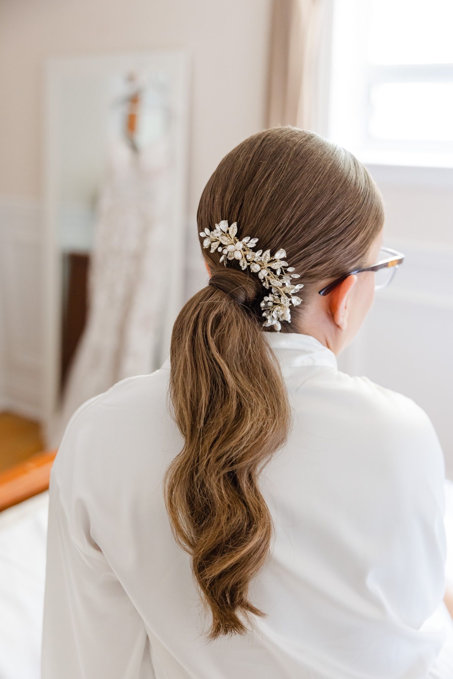 Close up of an elegant bridal hairstyle featuring a crystal hair accessory in a wavy ponytail.