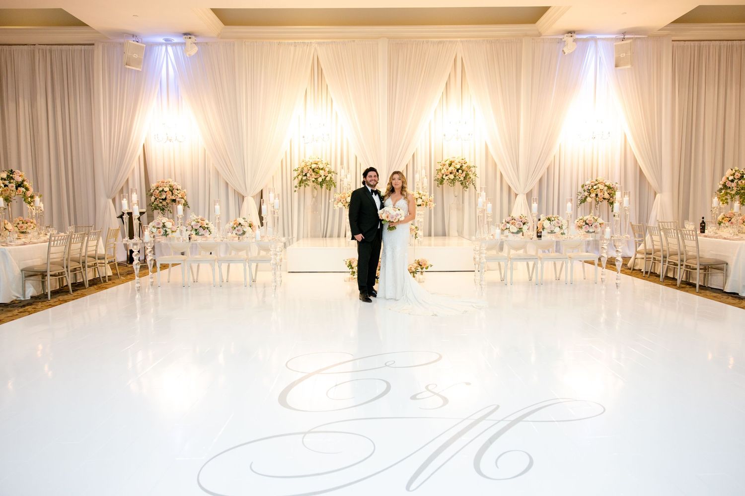 Elegant white wedding reception ballroom with draped fabric walls and monogrammed dance floor.