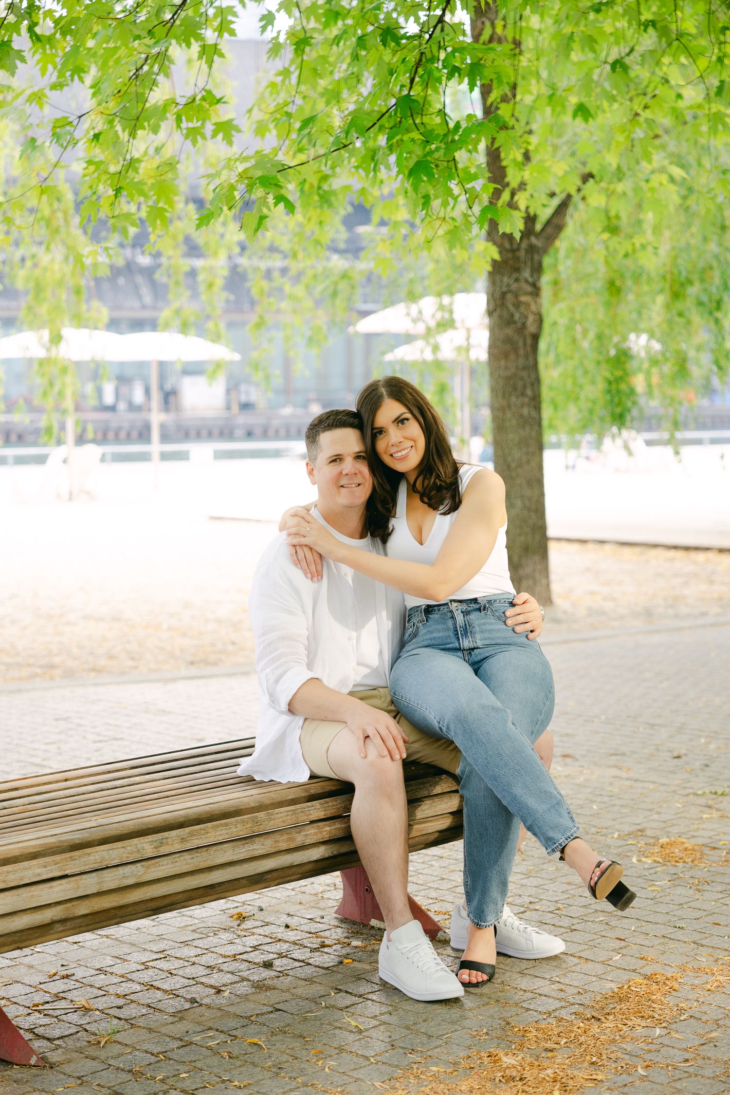 A couple sharing a tender moment while sitting on a wooden bench under green trees.