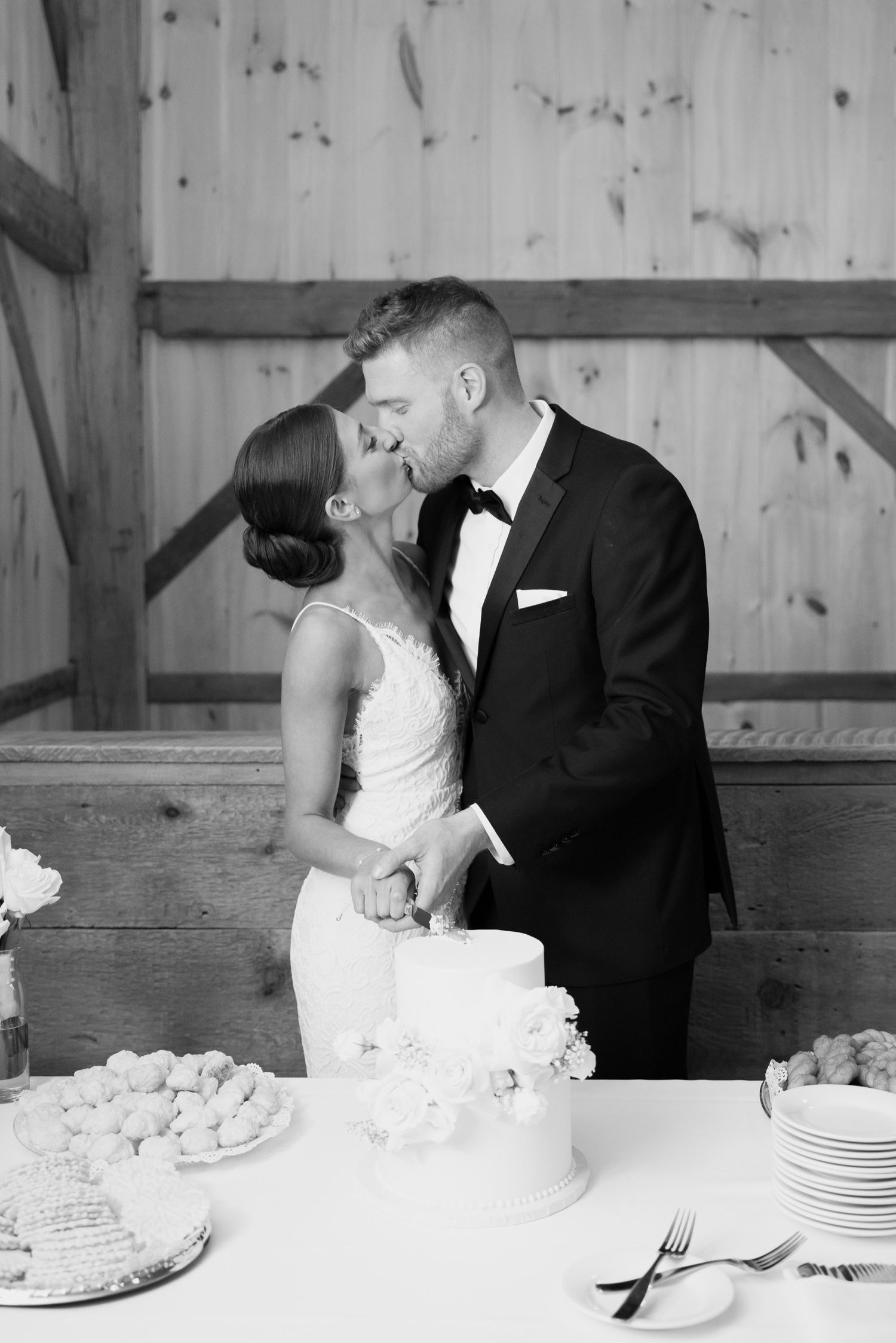 Intimate moment between couple while cutting their white wedding cake in a rustic wooden venue.