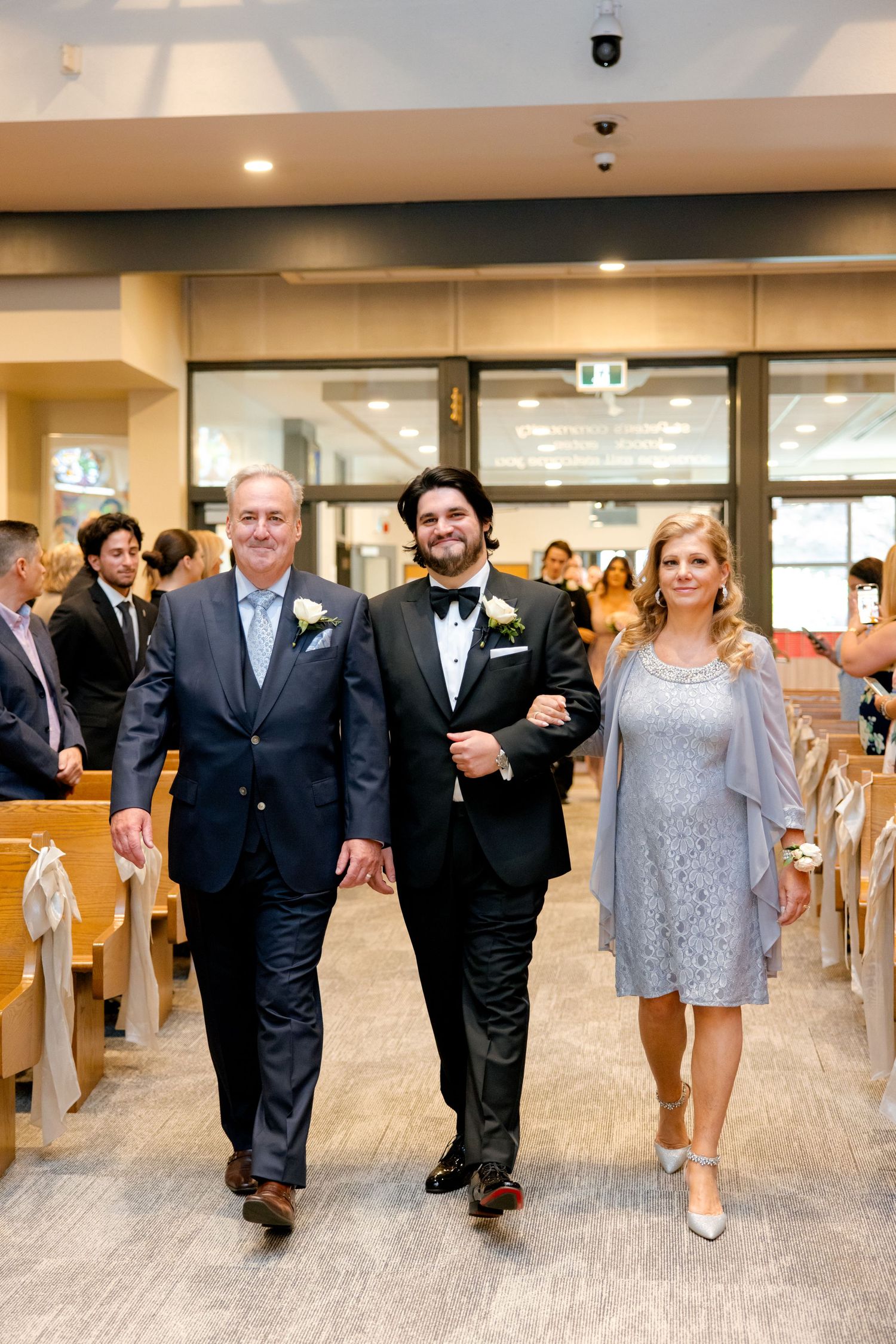 Wedding ceremony entrance in modern church hall with guests seated in wooden chairs.