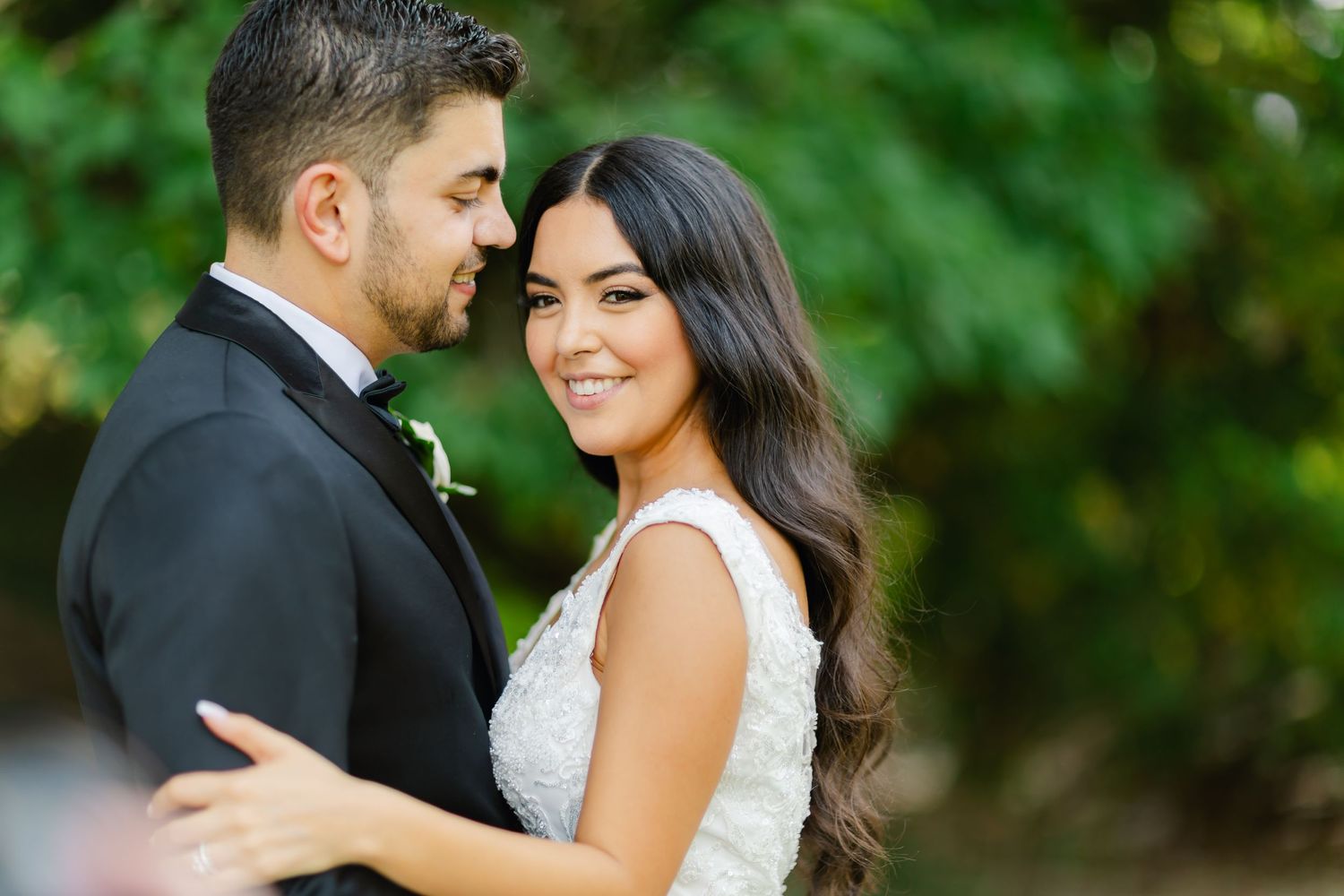 Joyful wedding couple shares a loving moment in front of lush green garden backdrop.