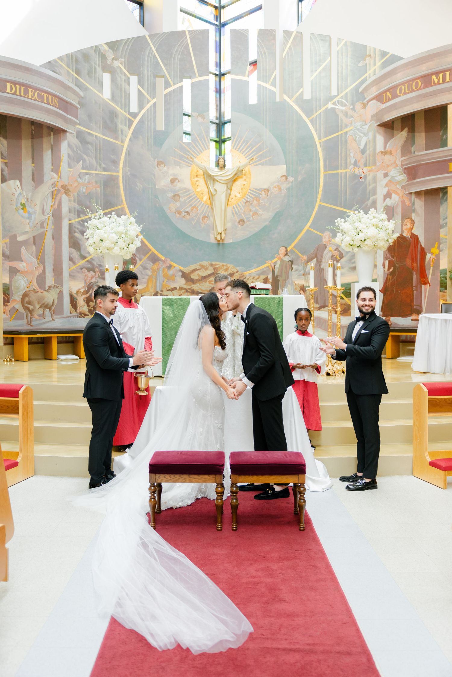 A wedding ceremony in a Catholic church featuring beautiful religious artwork and white floral arrangements.
