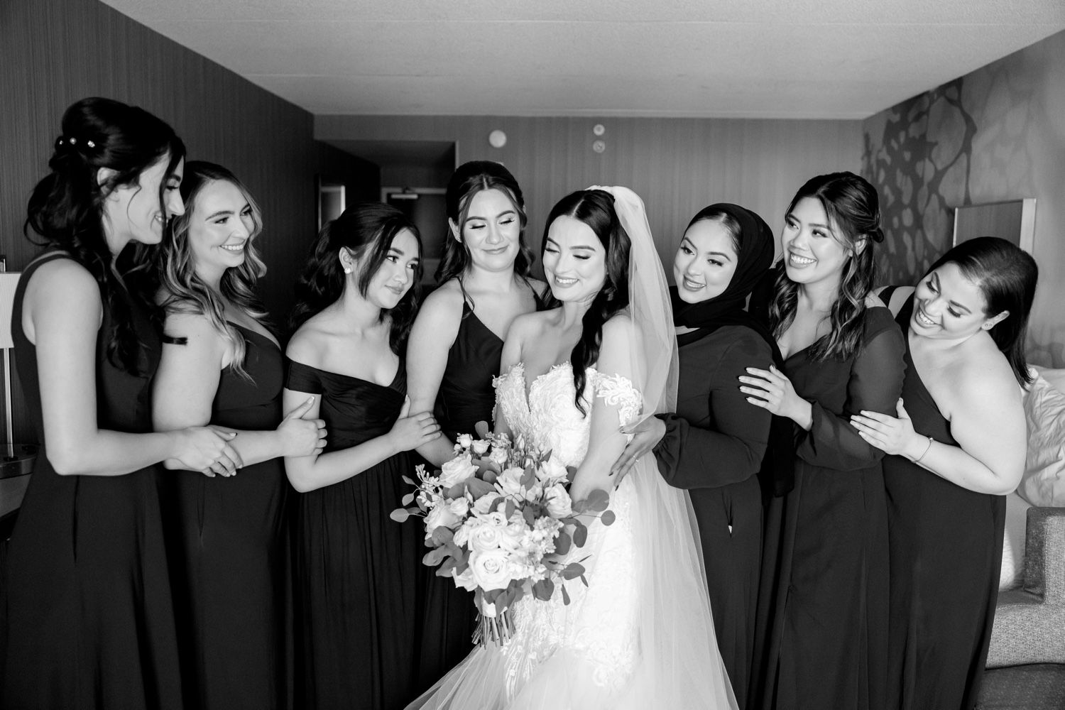 Wedding party gathered in a circle shares laughter and excitement during black and white moment.