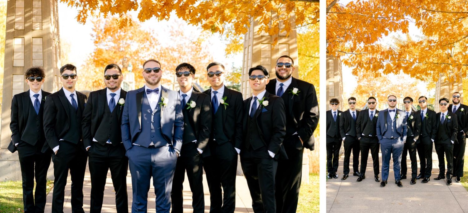 Groomsmen wearing sunglasses and dark suits pose confidently under fall foliage.