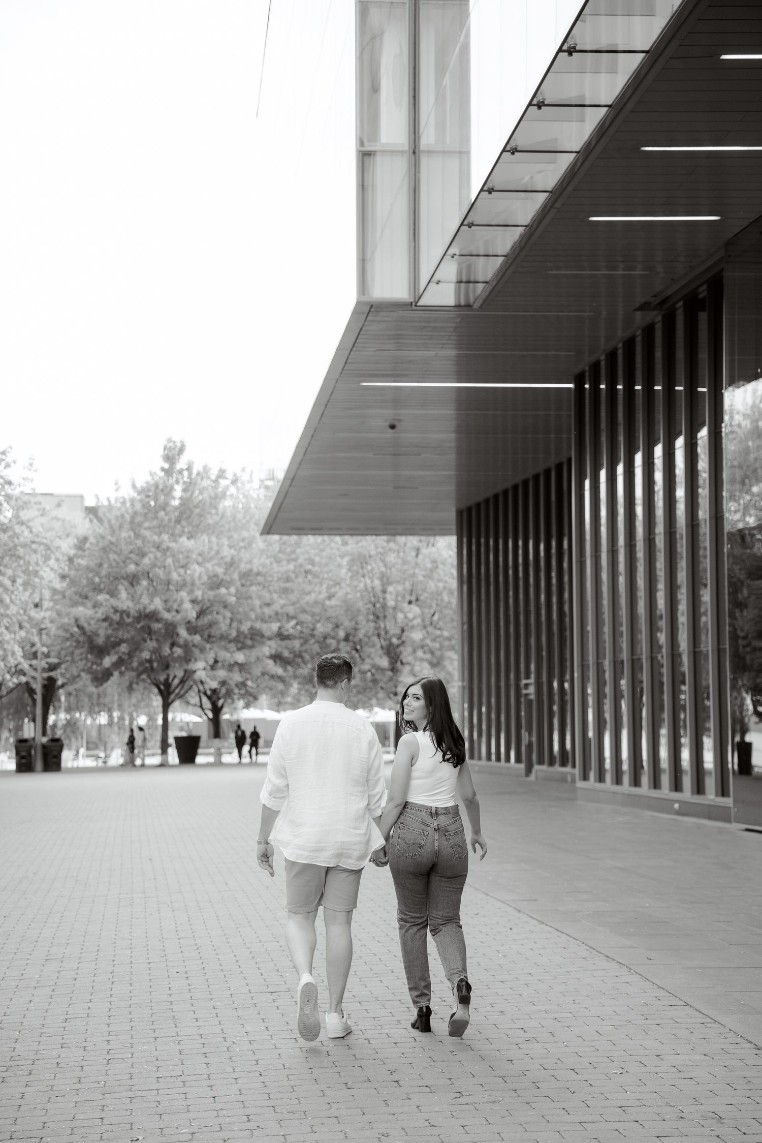 A black and white image showing a couple walking together near a contemporary architecture.
