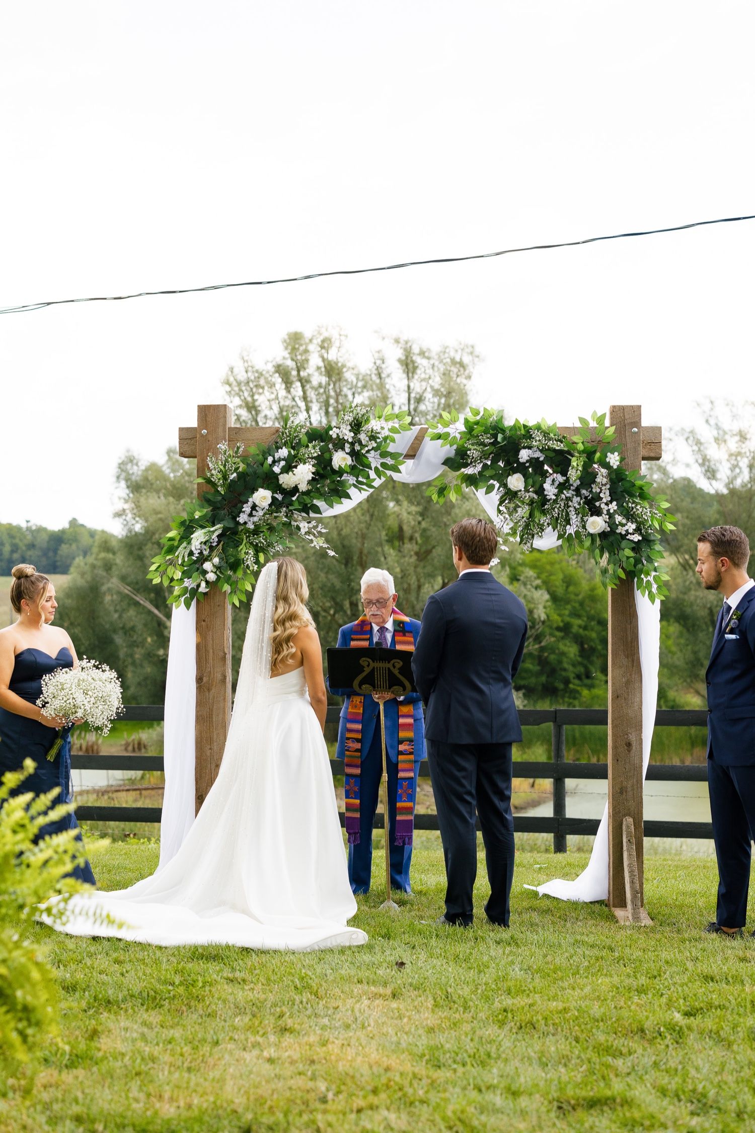 Wedding ceremony under a wooden arch decorated with white flowers and greenery.