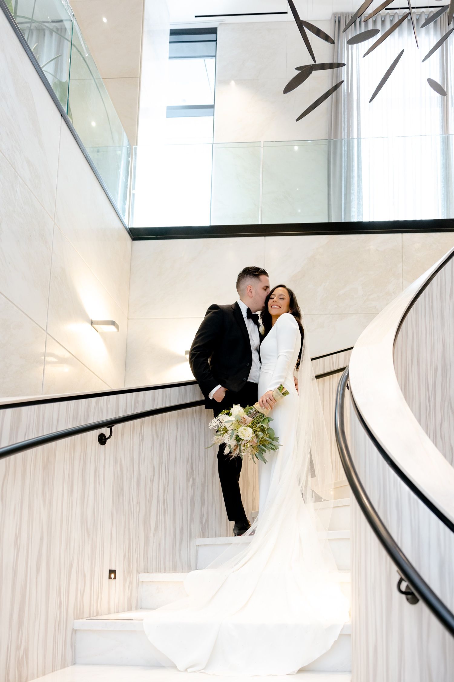 Elegant wedding portrait on modern white spiral staircase with dramatic architectural features.