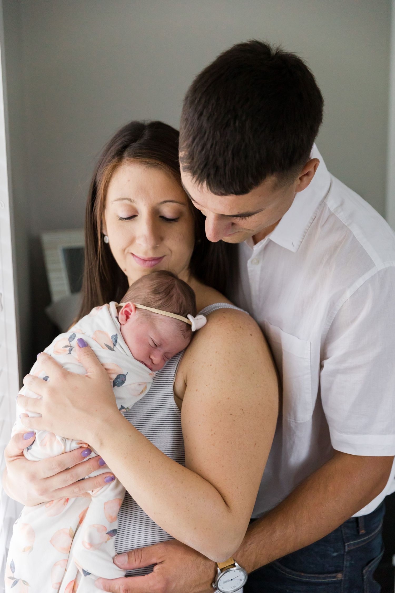 Tender moment between parents and newborn by window.