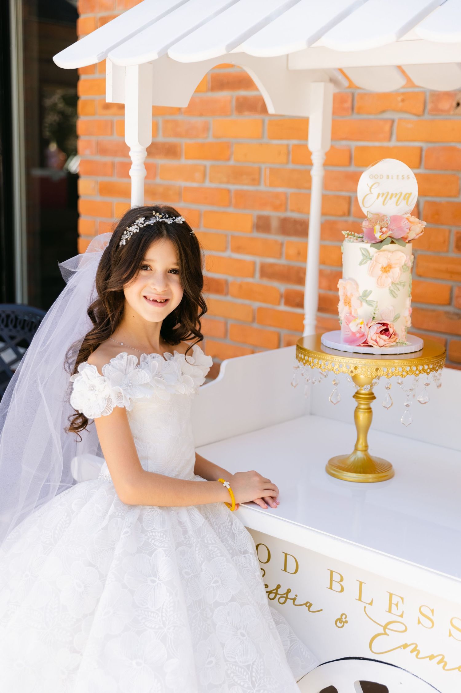 Elegant white dessert cart with decorative cakes against a red brick wall.