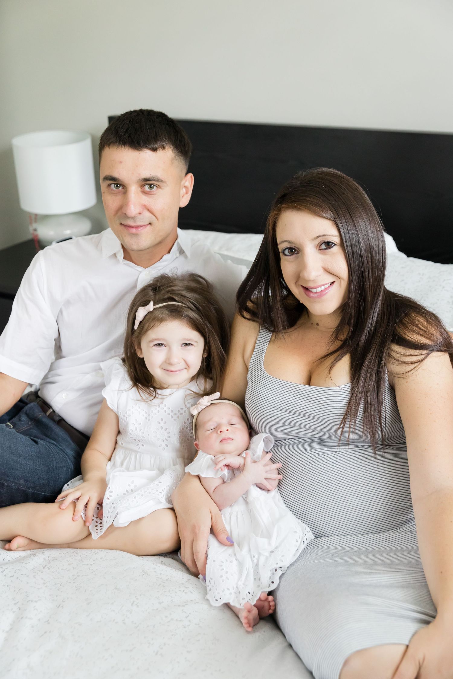 Loving family relaxing on bed together, wearing coordinated white and gray outfits.