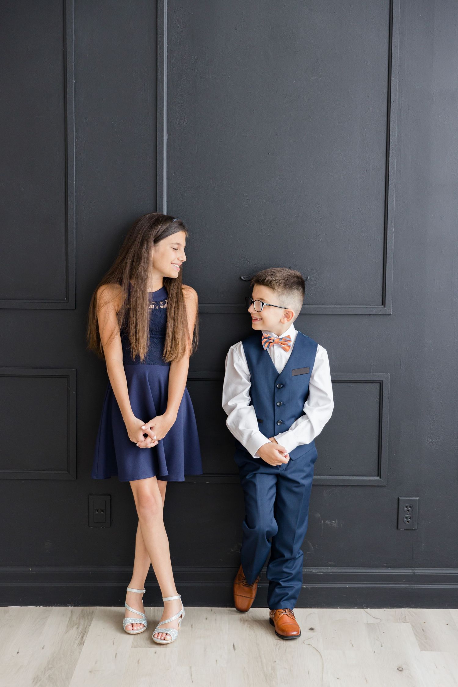 Charming formal portrait against dark wall featuring coordinated navy blue outfits.