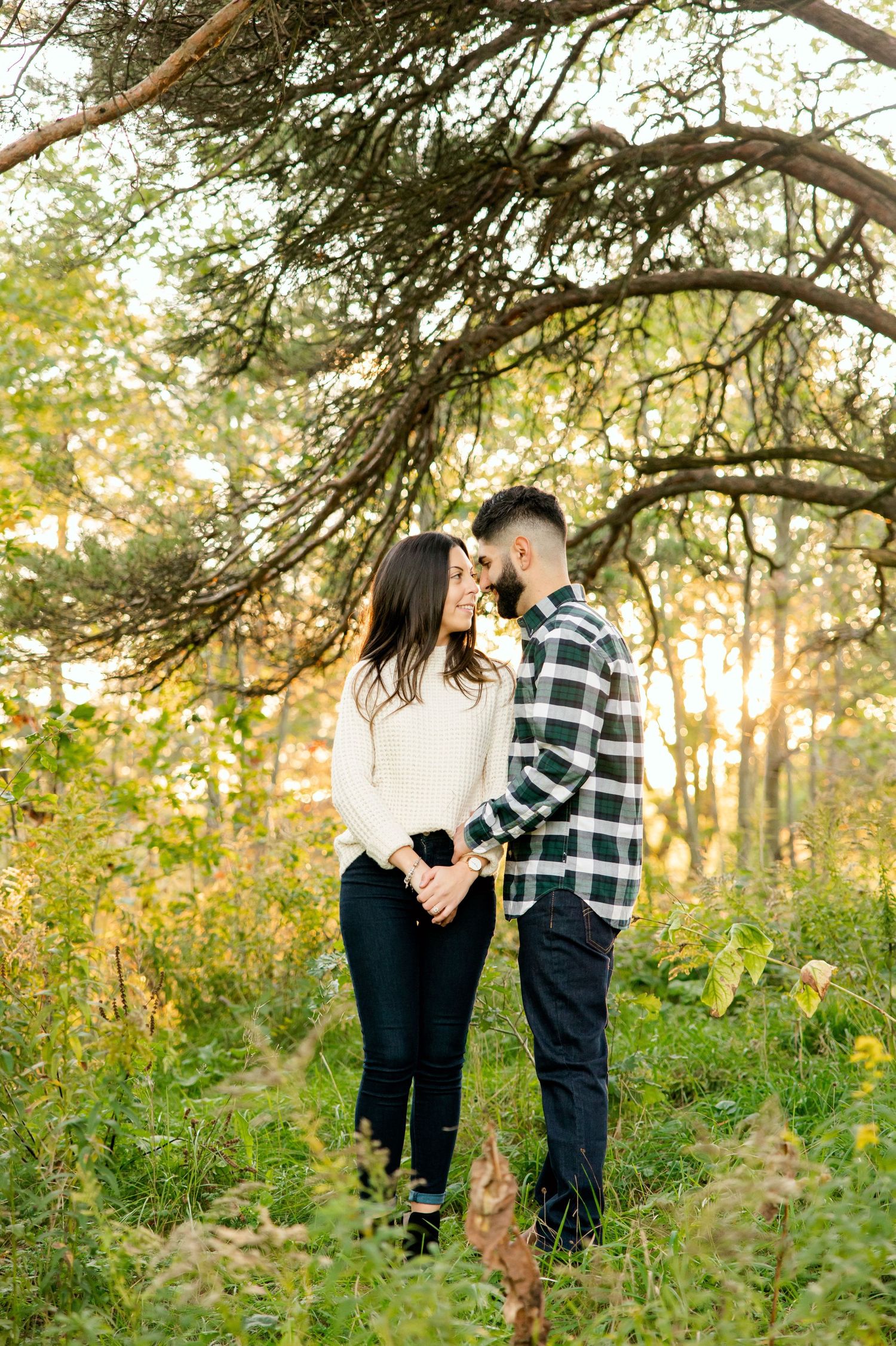 Couple in casual autumn outfits standing together on a wooded trail during golden hour.