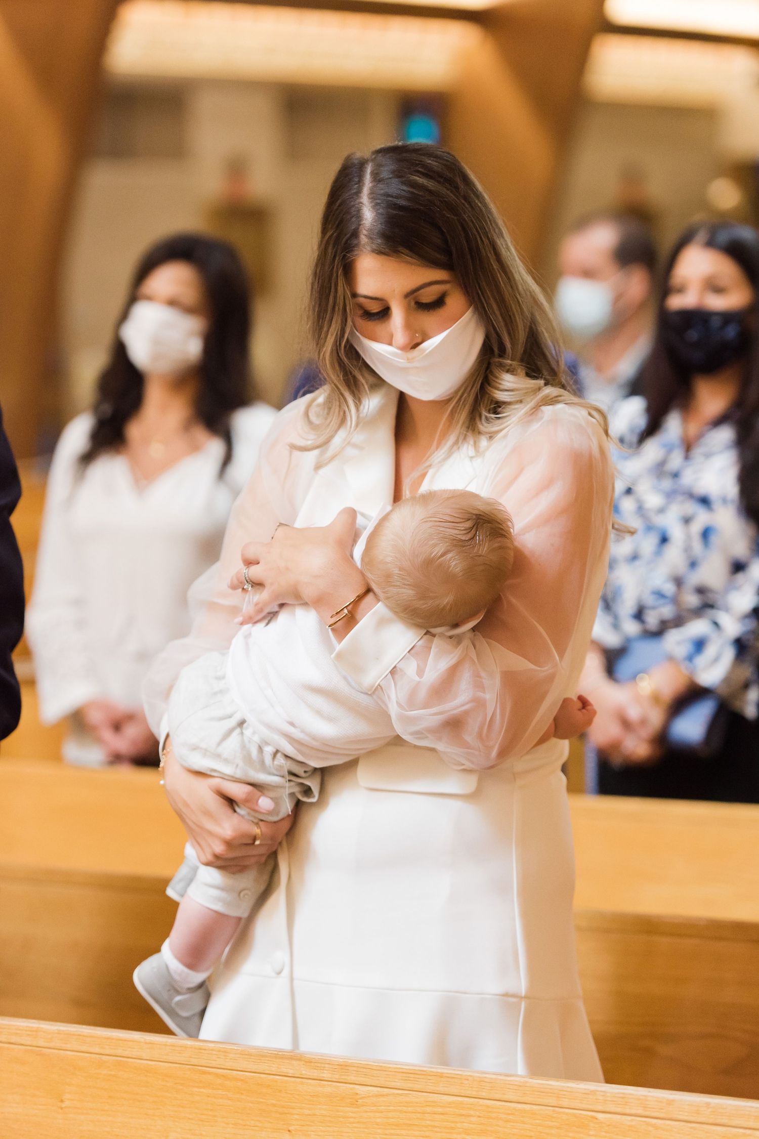 Baby in white baptismal outfit being cradled during church ceremony.