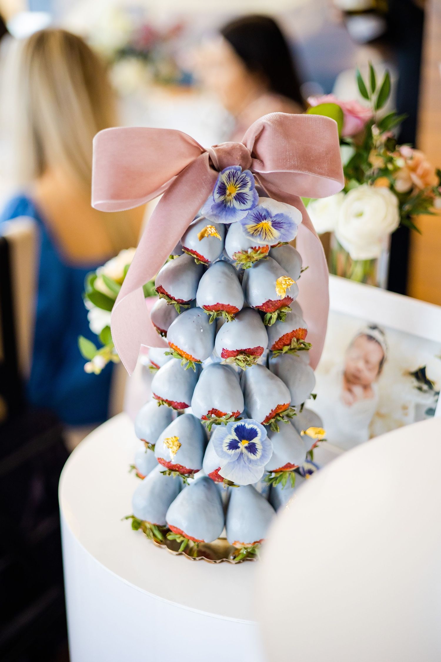 Tower of blue macarons decorated with pink bow and floral accents on white pedestal.