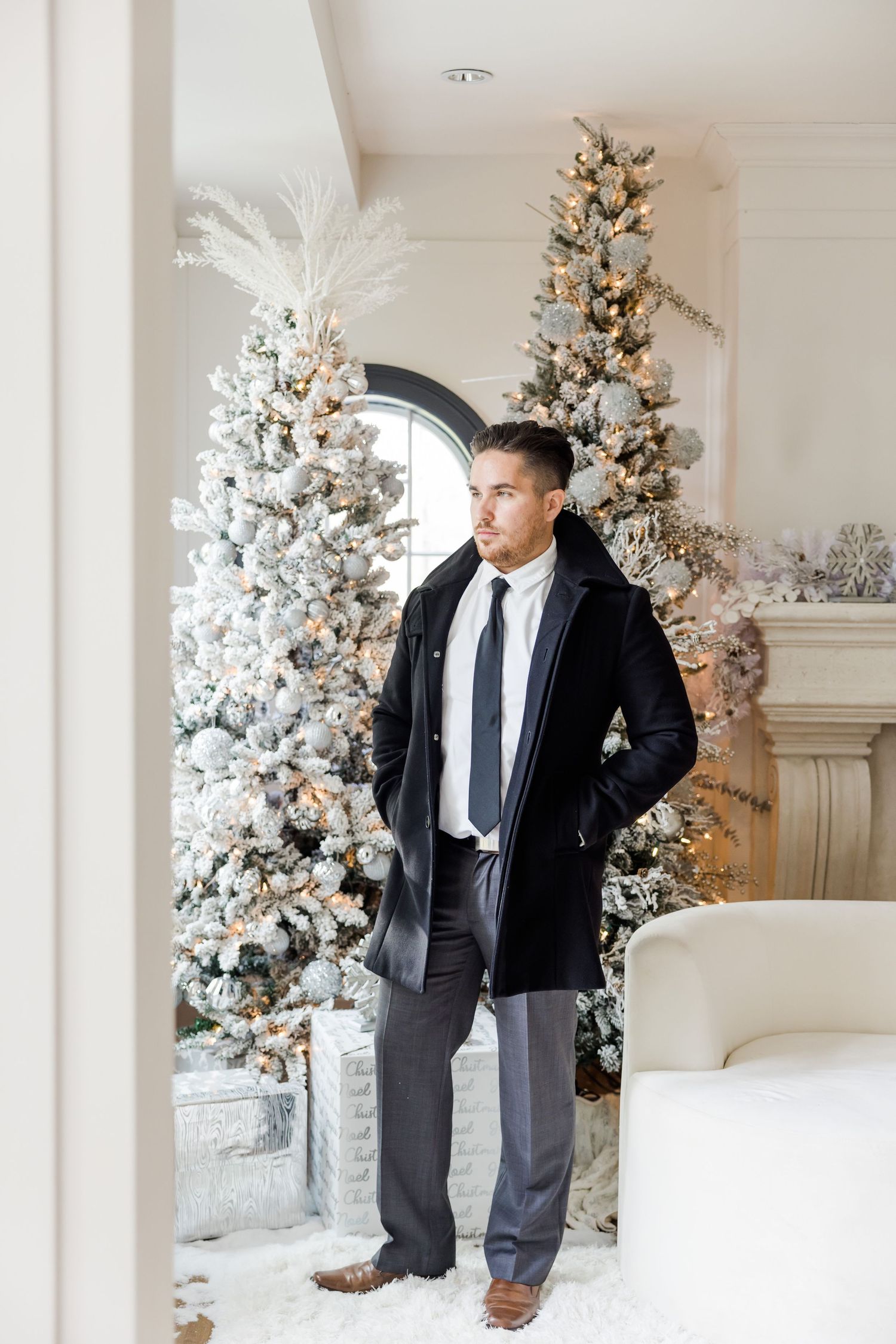 Holiday portrait featuring dark winter coat and suit next to snow-covered Christmas trees.