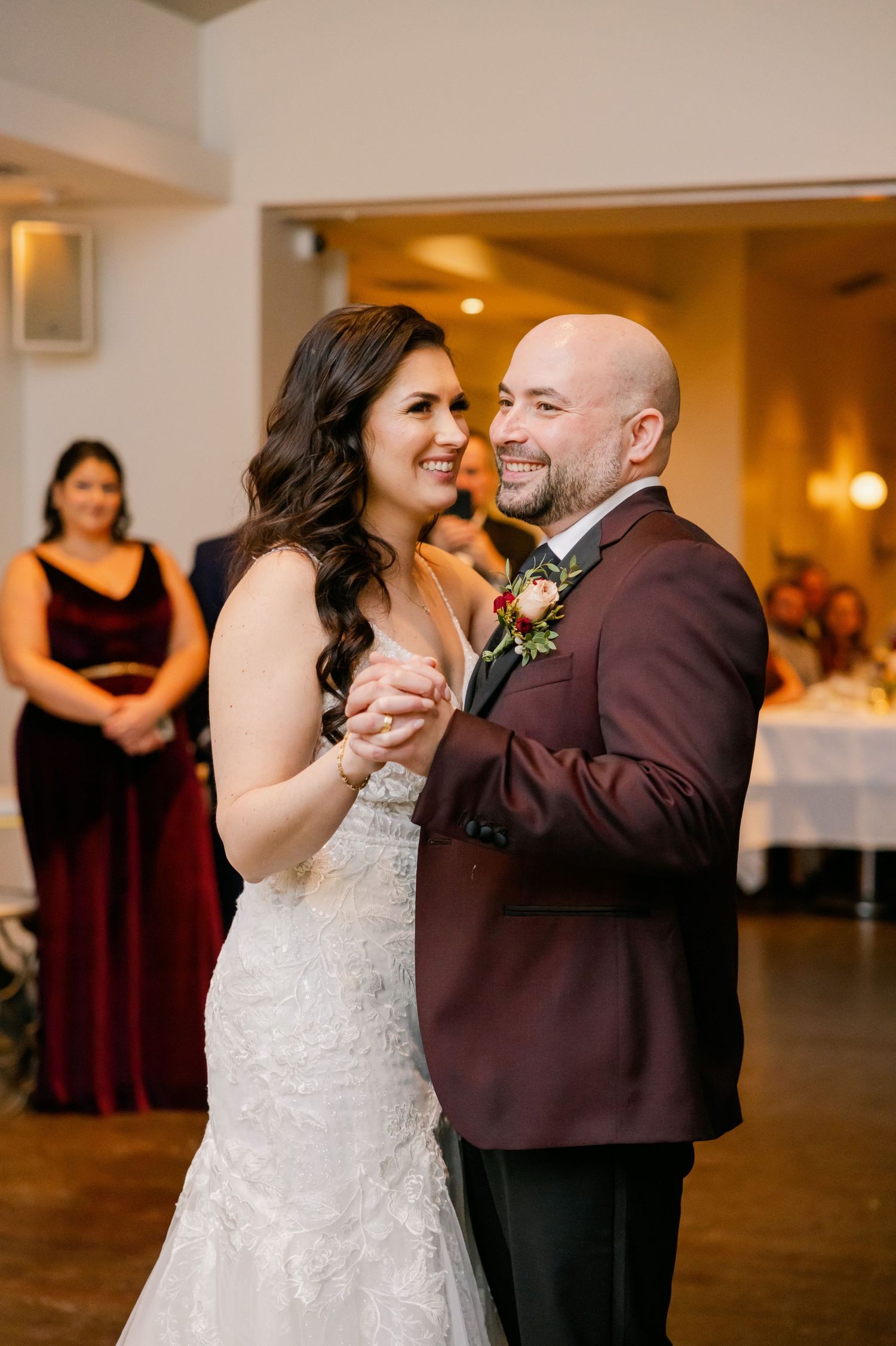 Romantic first dance moment at wedding reception with guests watching in background.