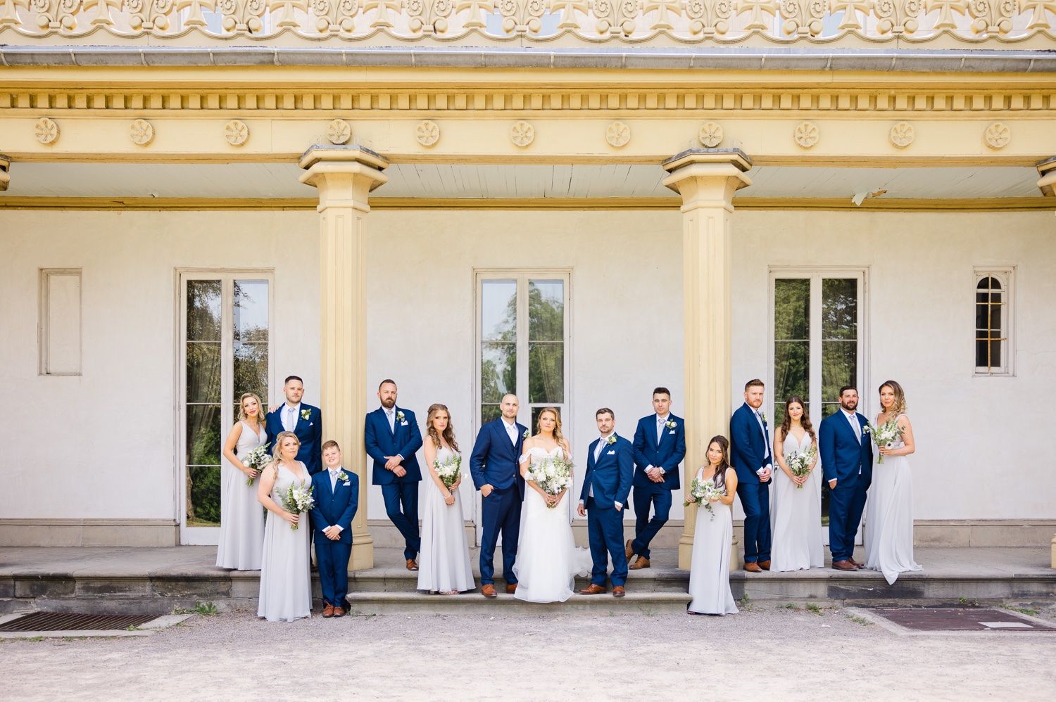 Wedding party in navy suits and light gray dresses poses against a classical columned building.