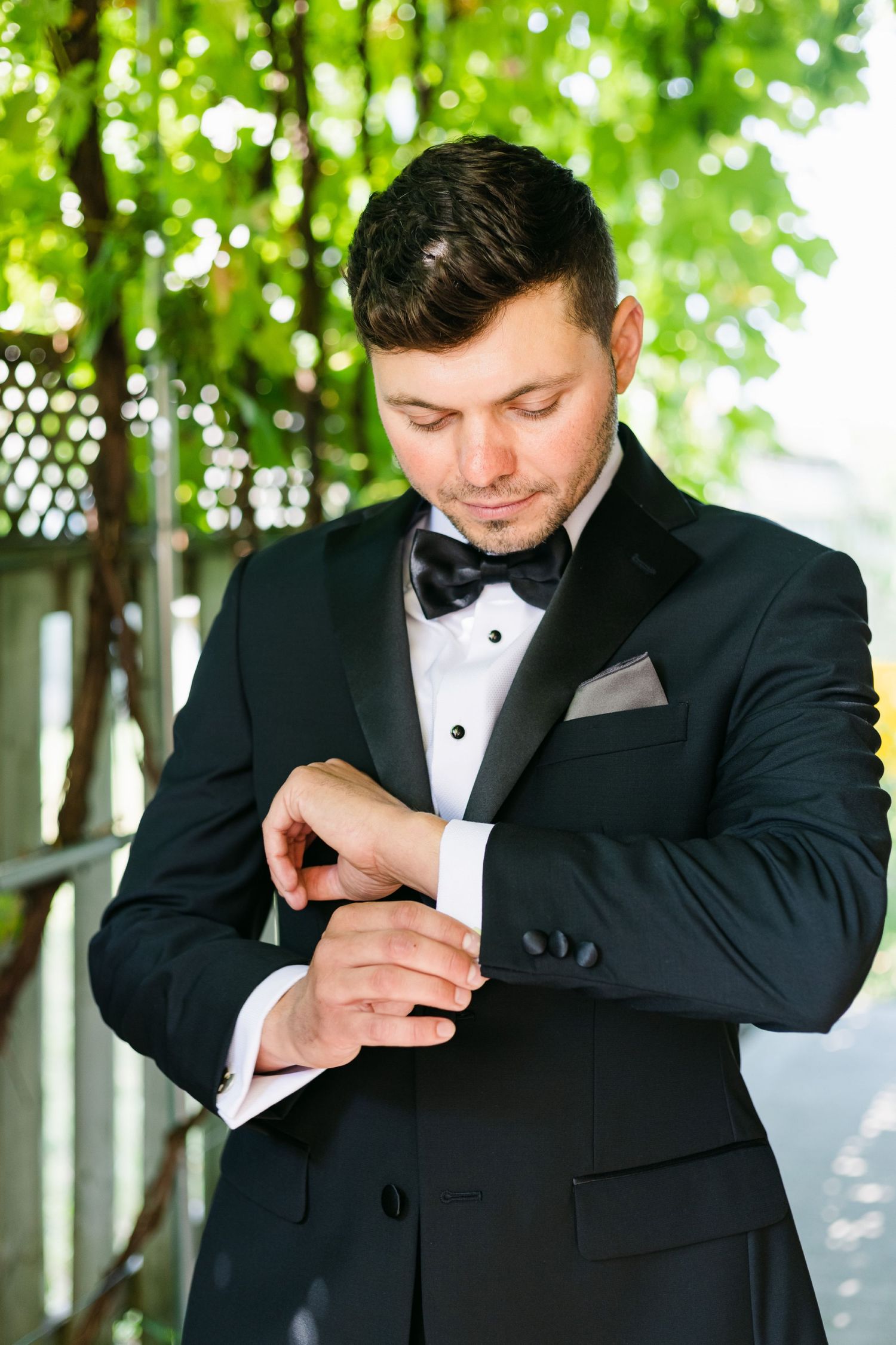 Close-up of formal attire highlighting black tuxedo jacket, bow tie and cuff adjustments.