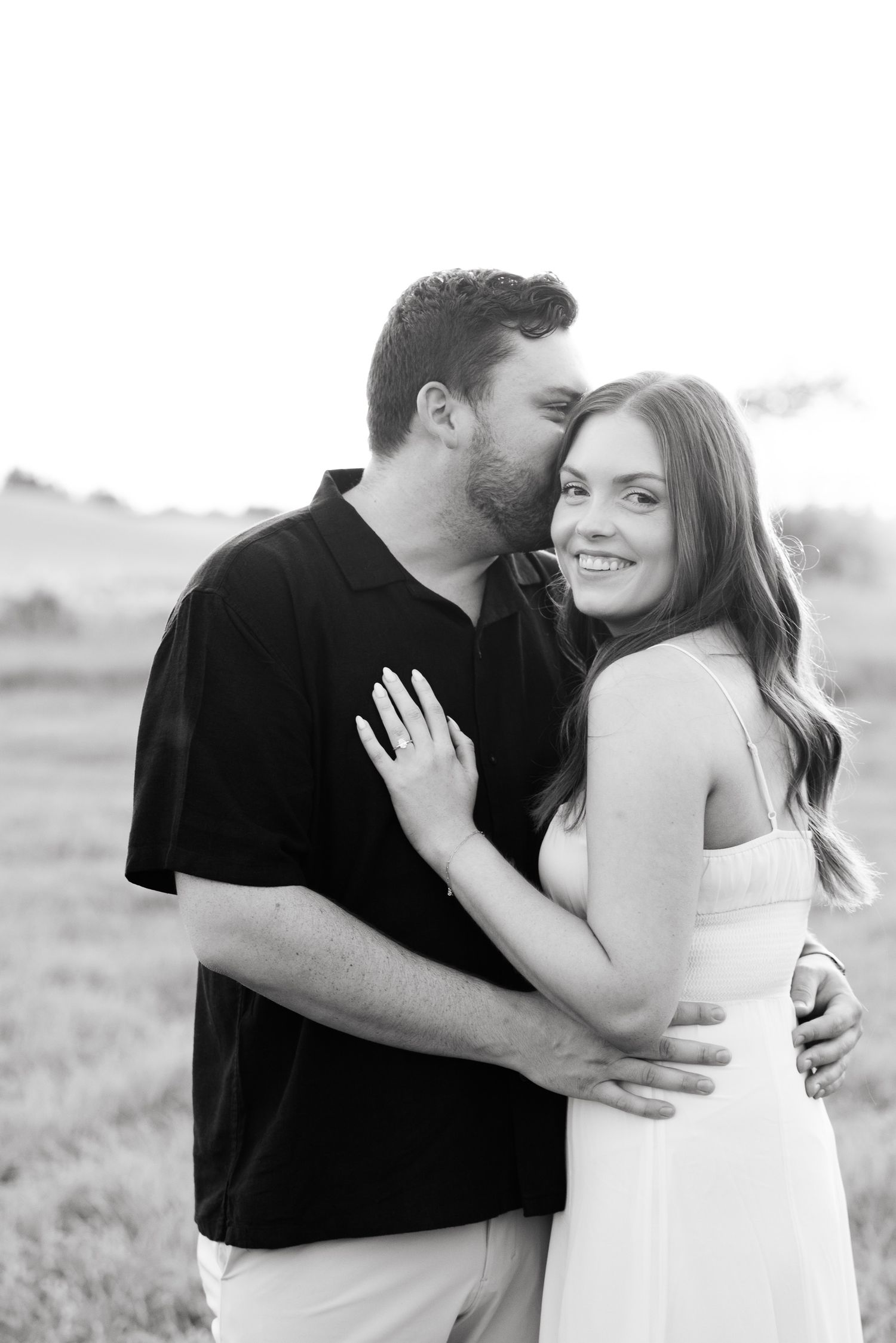 A black and white close-up of a couple sharing an intimate embrace outdoors.