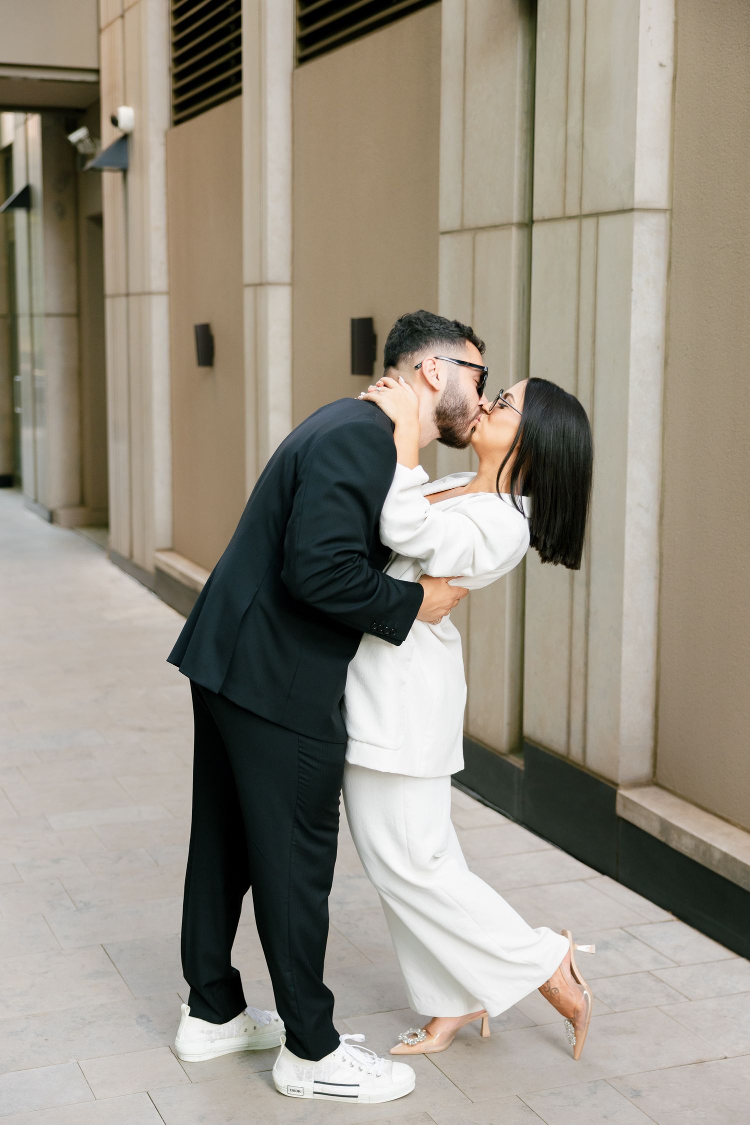 A couple in black and white outfits share a romantic kiss on an urban street.