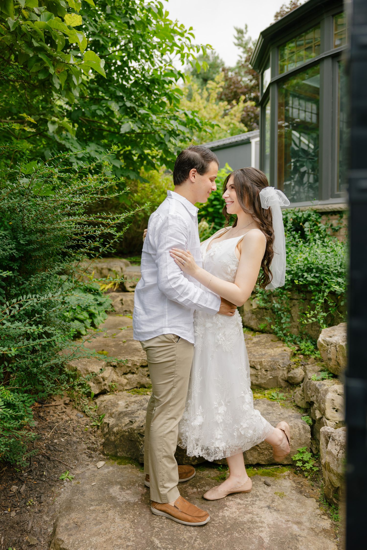 Casual elegant wedding portrait of couple standing on stone path surrounded by greenery.