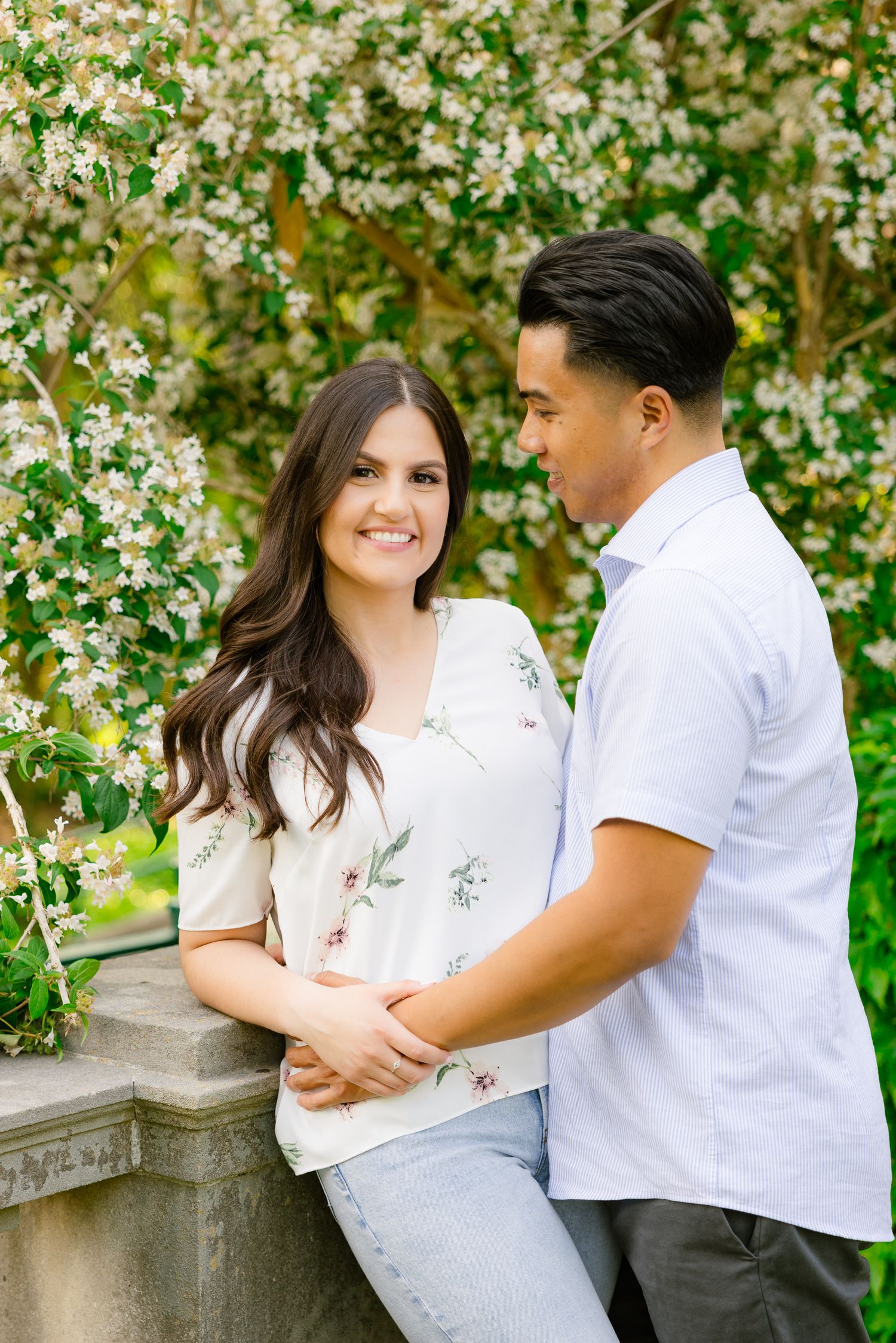 Couple shares tender moment against backdrop of blooming spring trees and stone architecture.