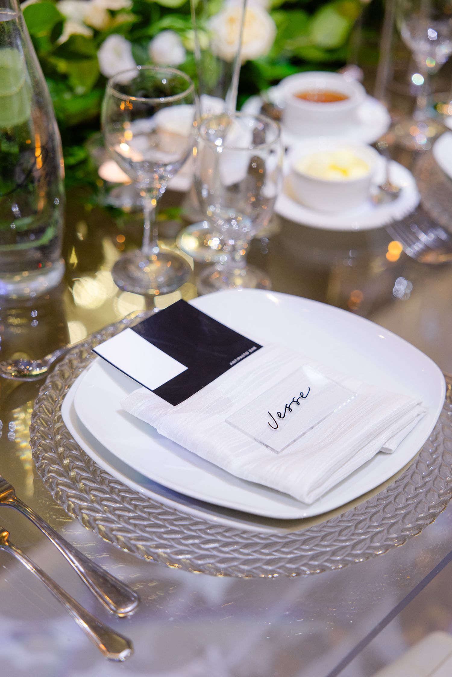 Elegant place setting with crystal charger plate, black and white menu card, and white napkin.