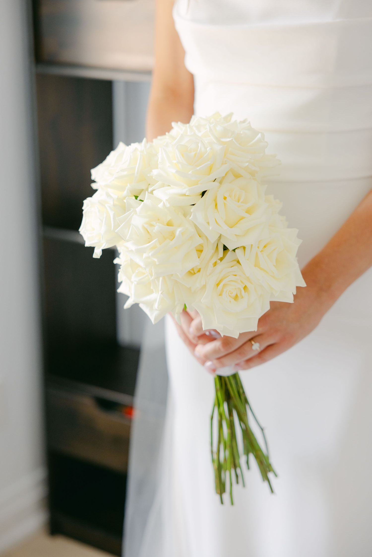 A stunning white rose bouquet is held against a pure white wedding dress.