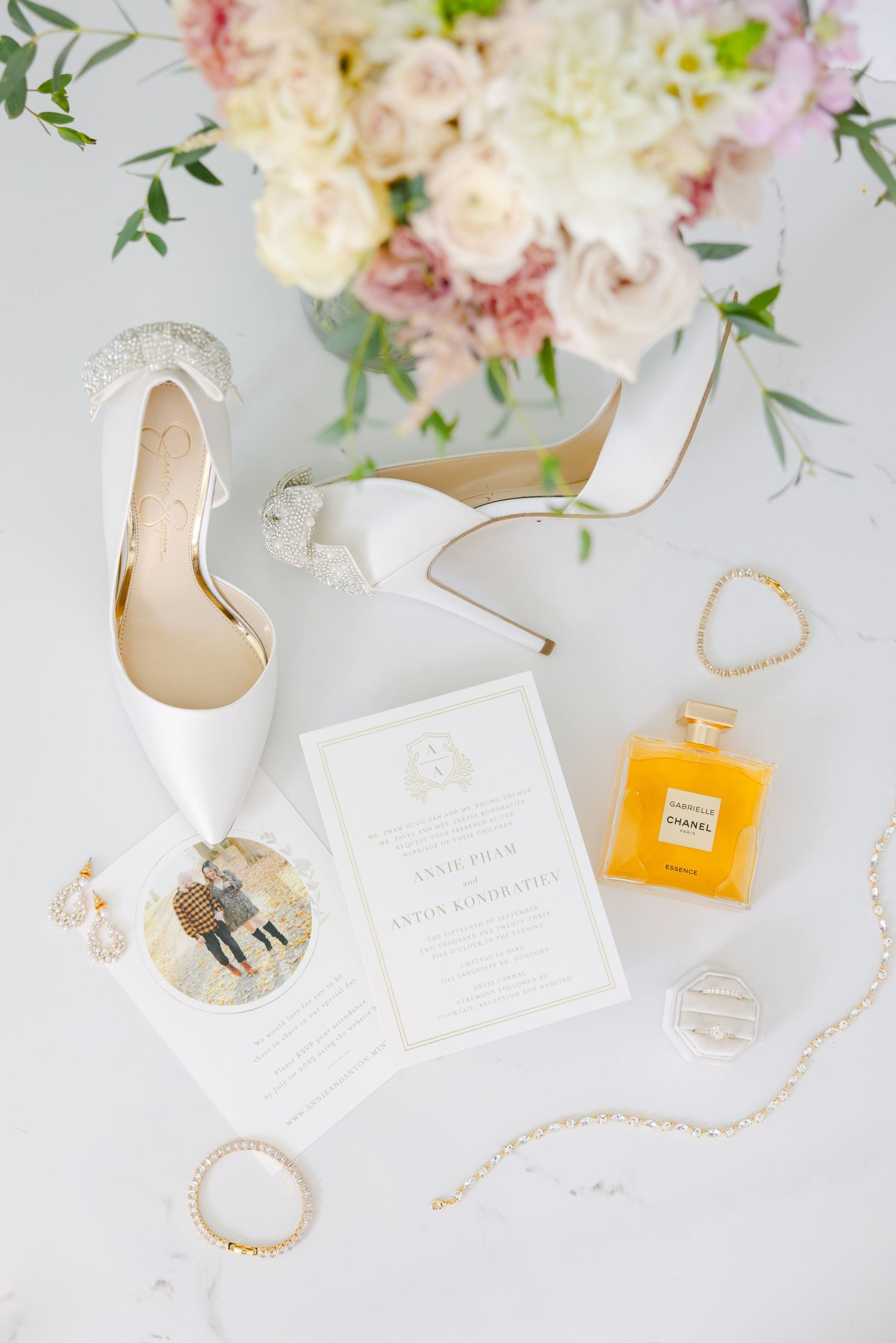 Wedding flatlay with white heels, floral arrangements, invitation and Chanel perfume.