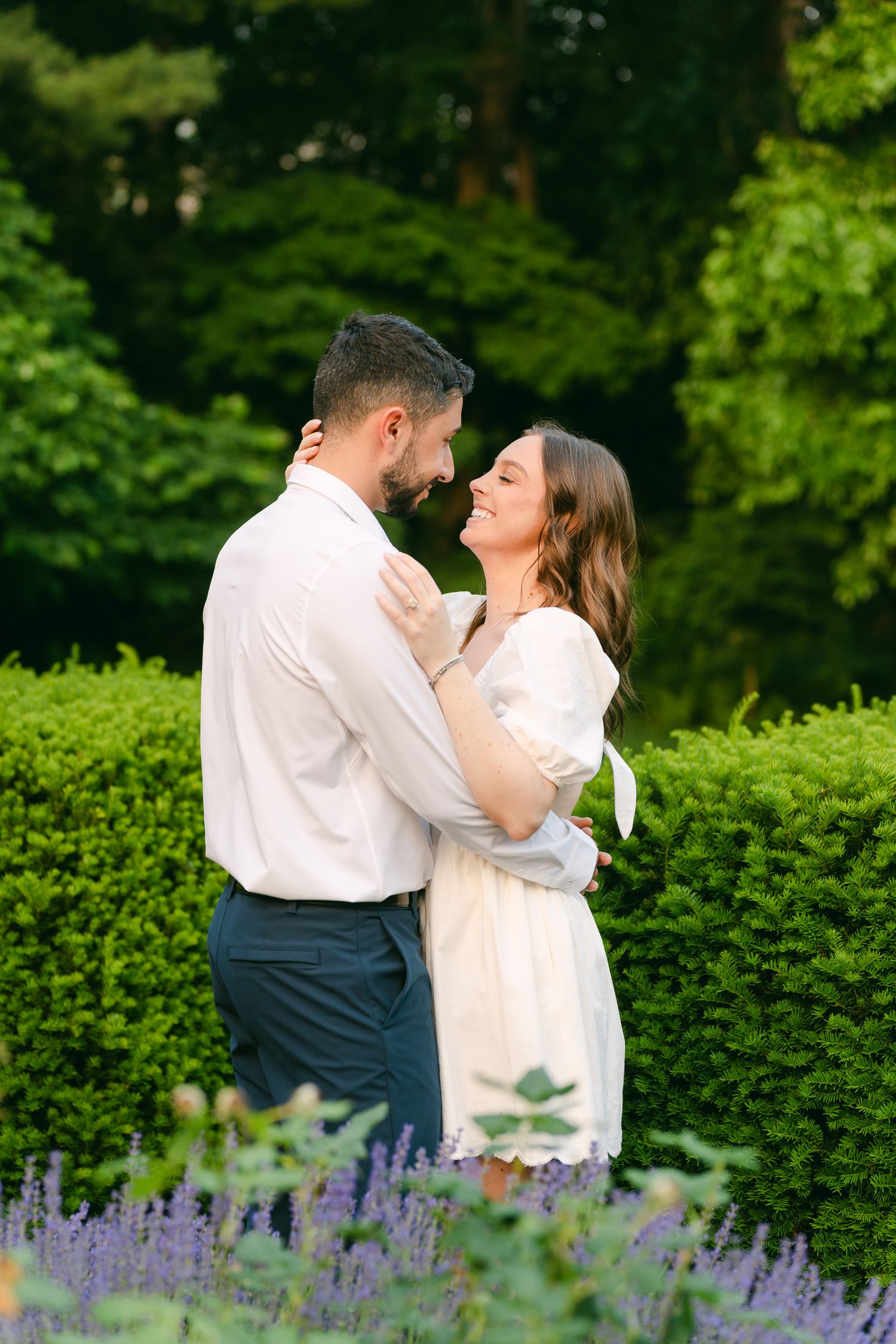 Couple in white and navy outfits share a romantic moment in a garden with lavender flowers.