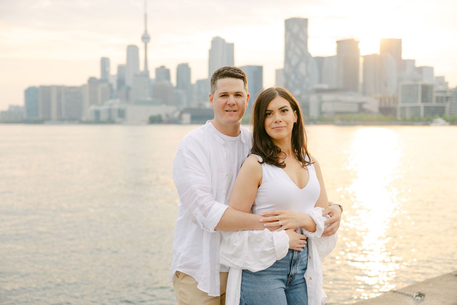 Couple poses along Lake Ontario with Toronto's downtown skyline glowing in evening light.