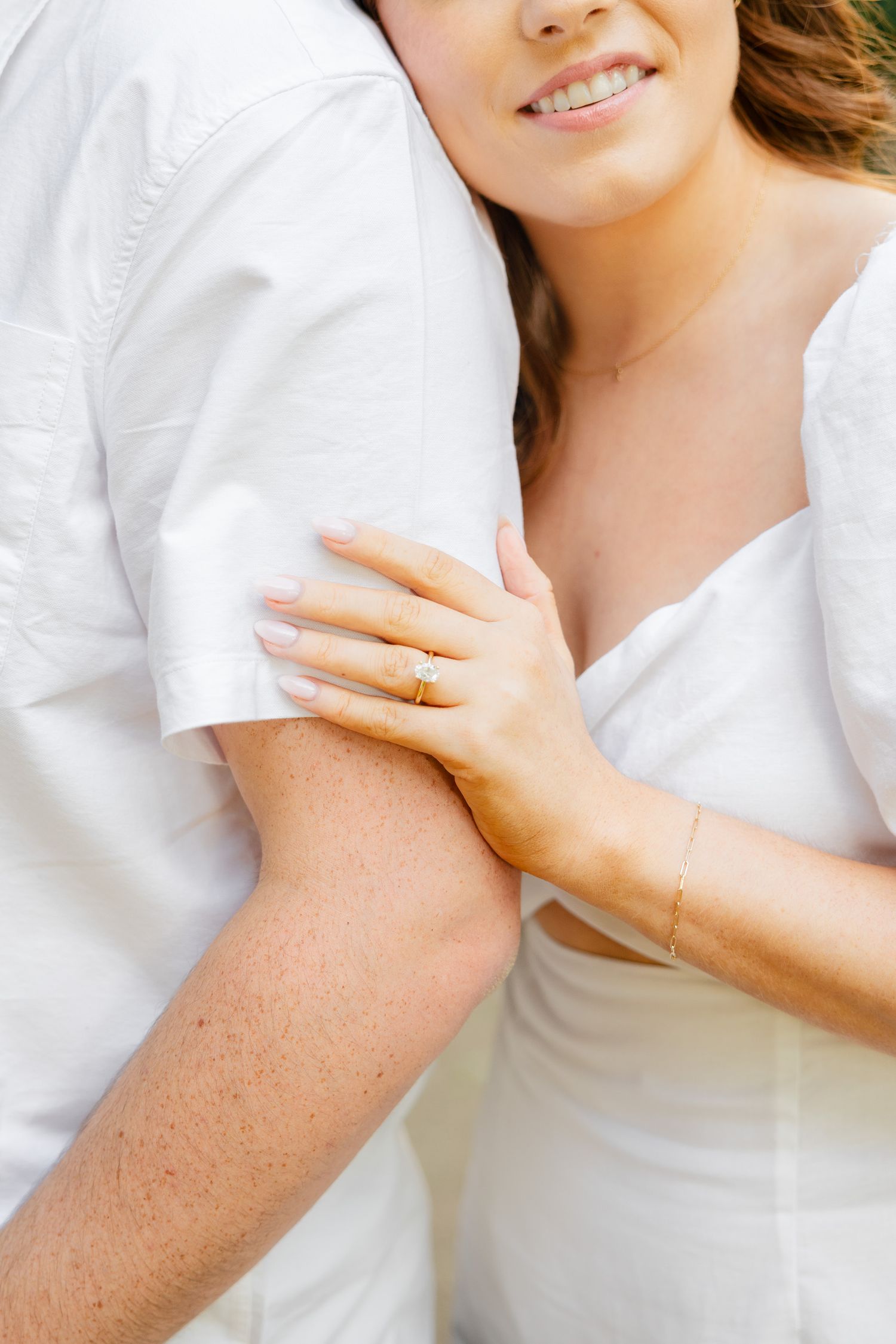 Close-up of hands embracing, showing a delicate gold ring and bracelet against white clothing.