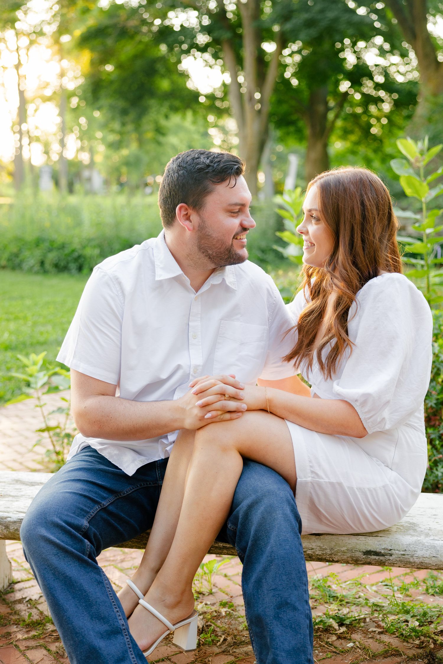 A romantic couple sits together on a stone bench in a lush garden setting at golden hour.