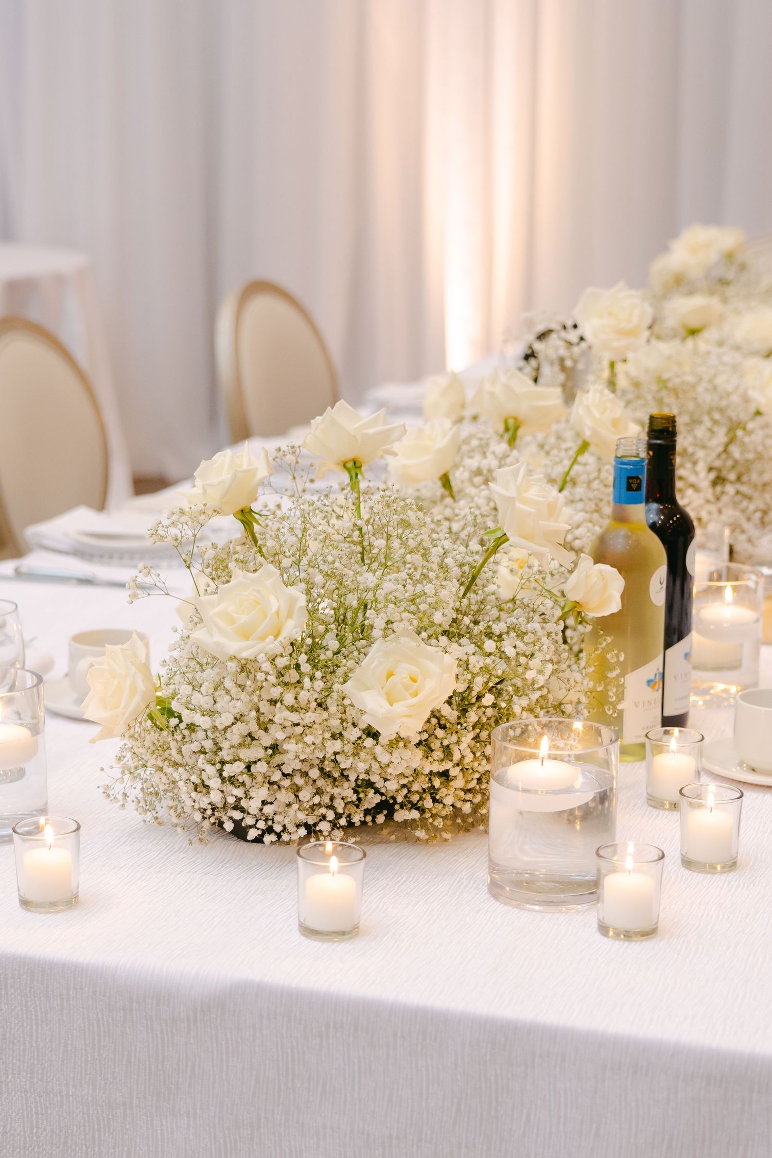 Romantic wedding table centerpiece with white roses, baby's breath, and glowing candles.
