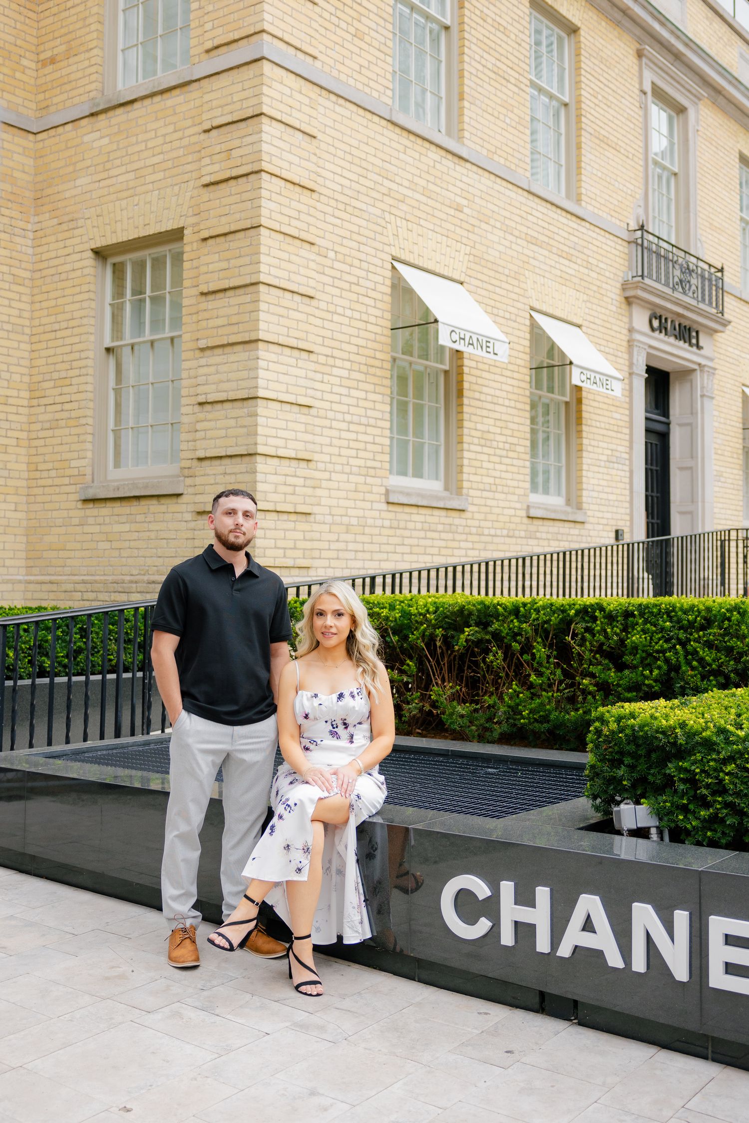 Couple posing outside luxury Chanel storefront with yellow brick facade.
