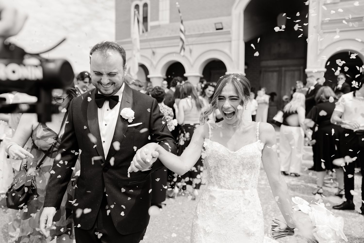 A happy couple walks through showering confetti outside a church after their wedding ceremony.