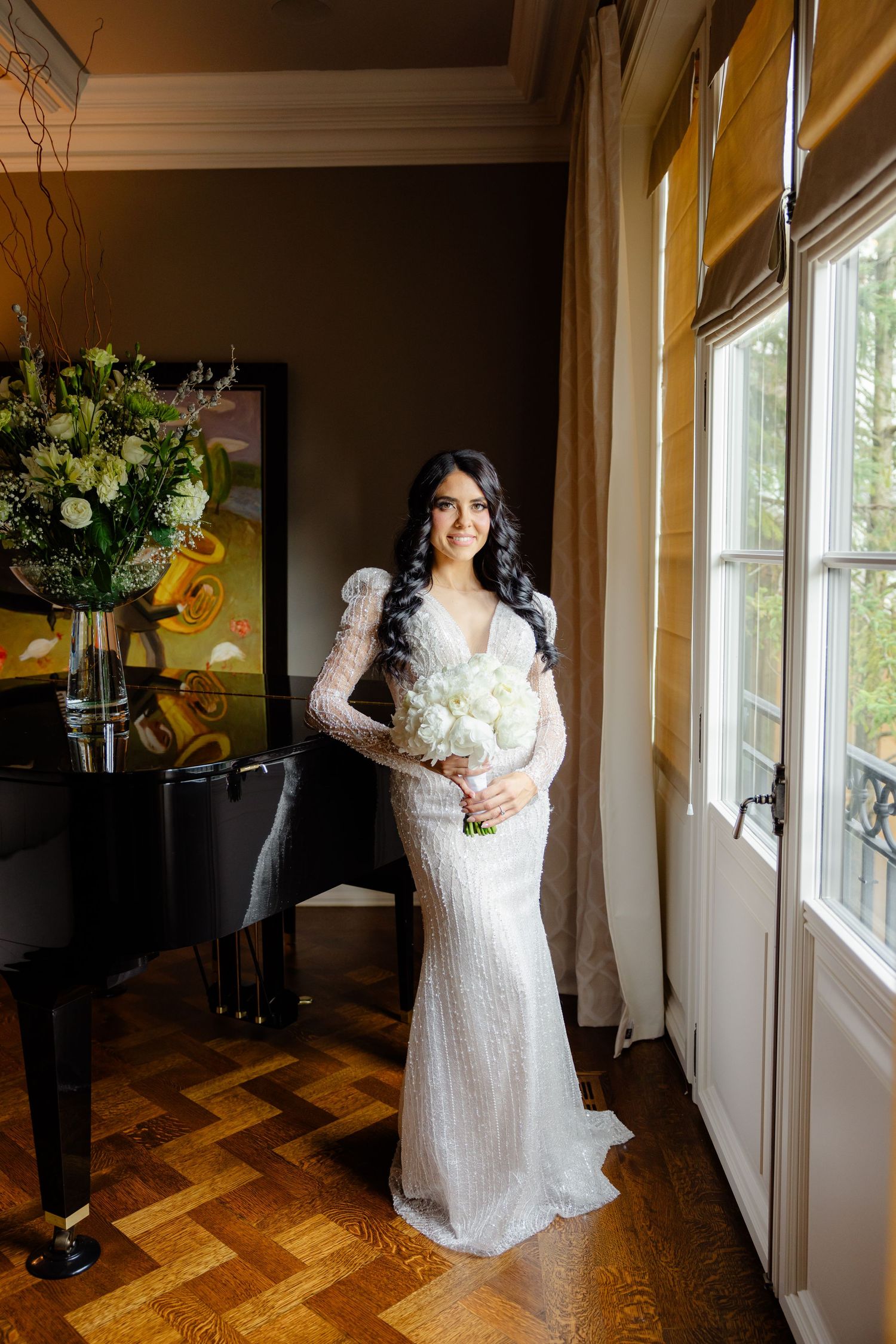 Full length bridal portrait showing a fitted white beaded gown against warm interior lighting.