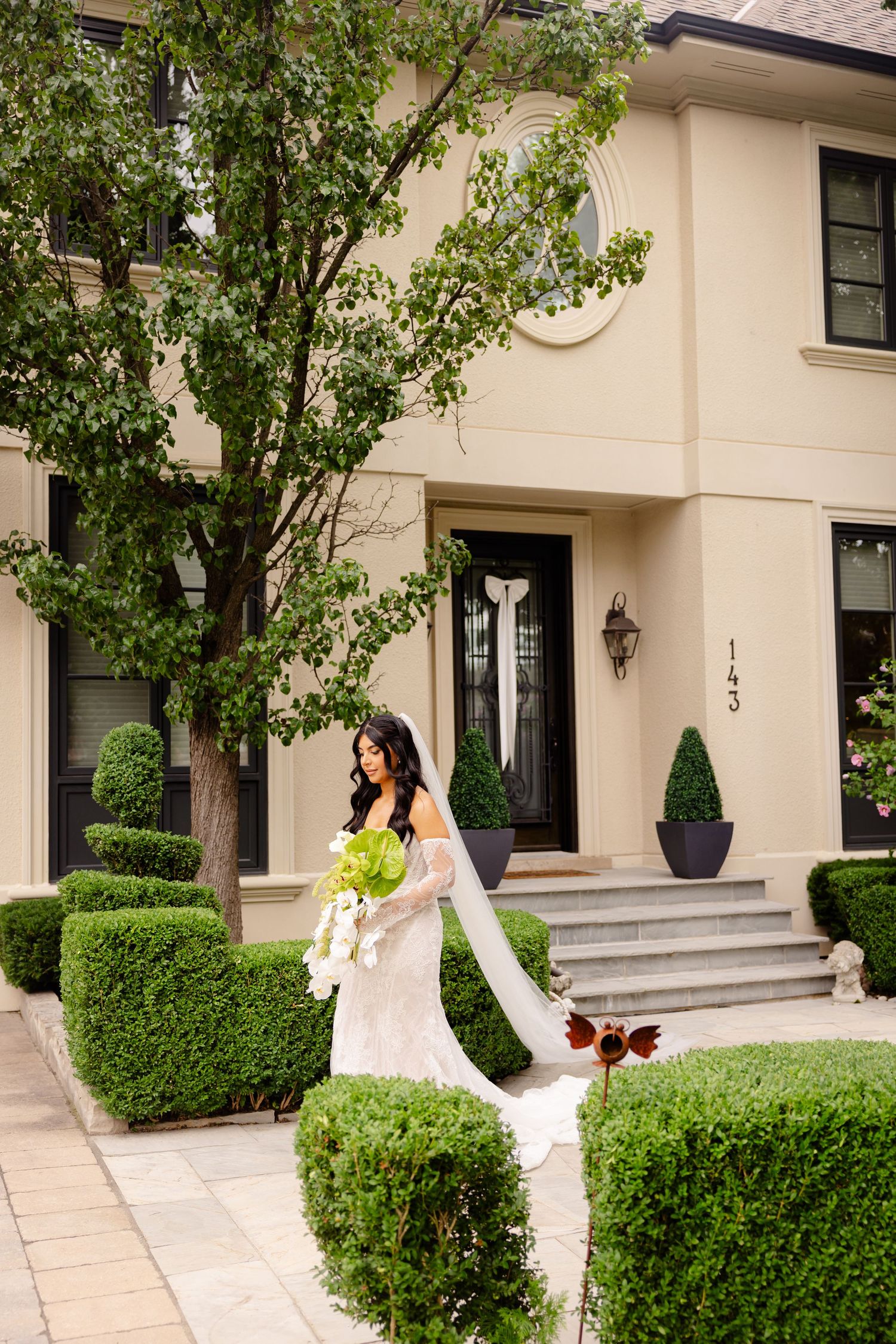 Elegant bridal portrait in front of a luxurious beige house with manicured hedges and a grand entrance.