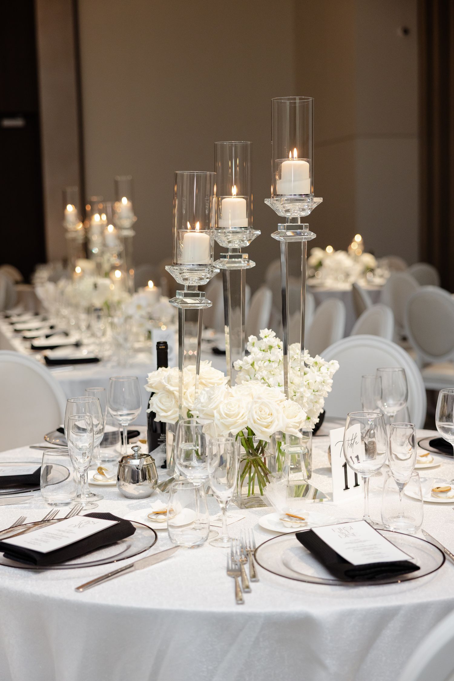Elegant white wedding table setting with tall glass candle holders, white floral centerpieces and formal place settings.