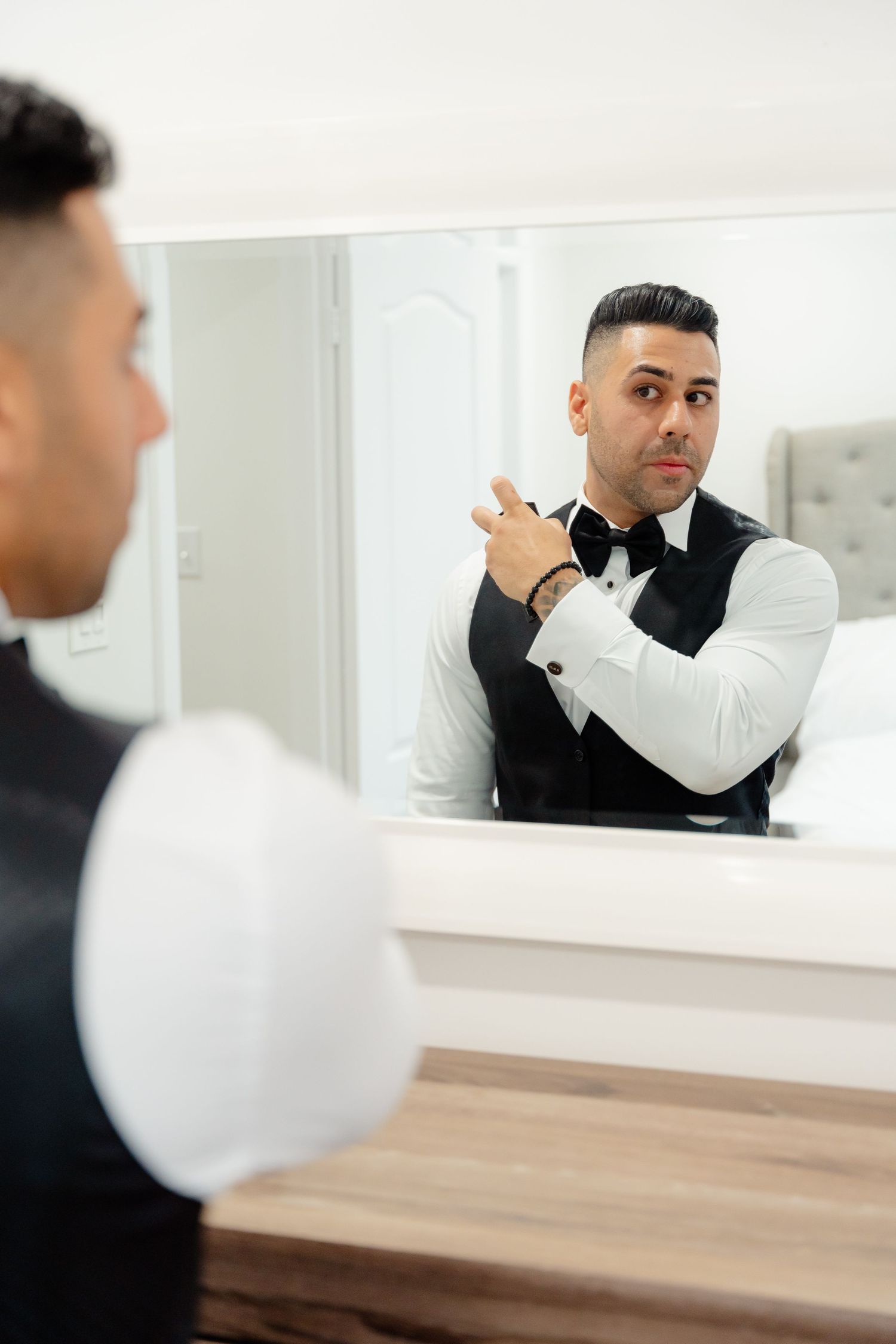 Person in formal vest adjusting cufflinks while looking in mirror.